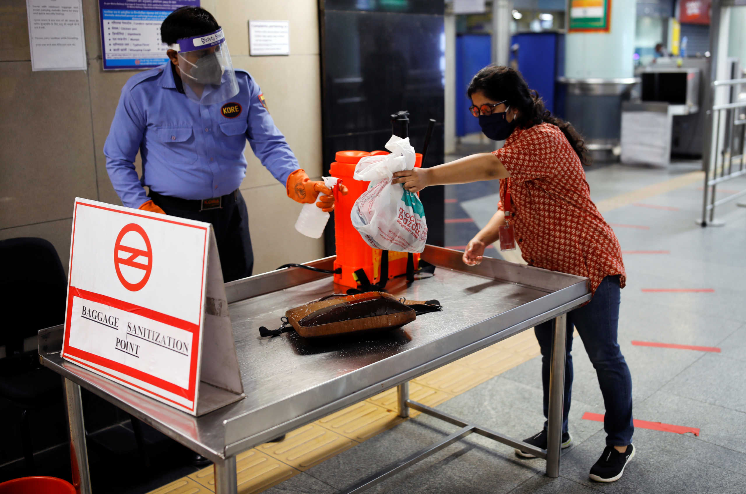 A security guard sprays disinfectant on a commuter's bag at a Delhi metro train station, on the first day of the restart of their operations, amidst the spread of coronavirus disease (COVID-19), in New Delhi, India, September 7, 2020. REUTERS
