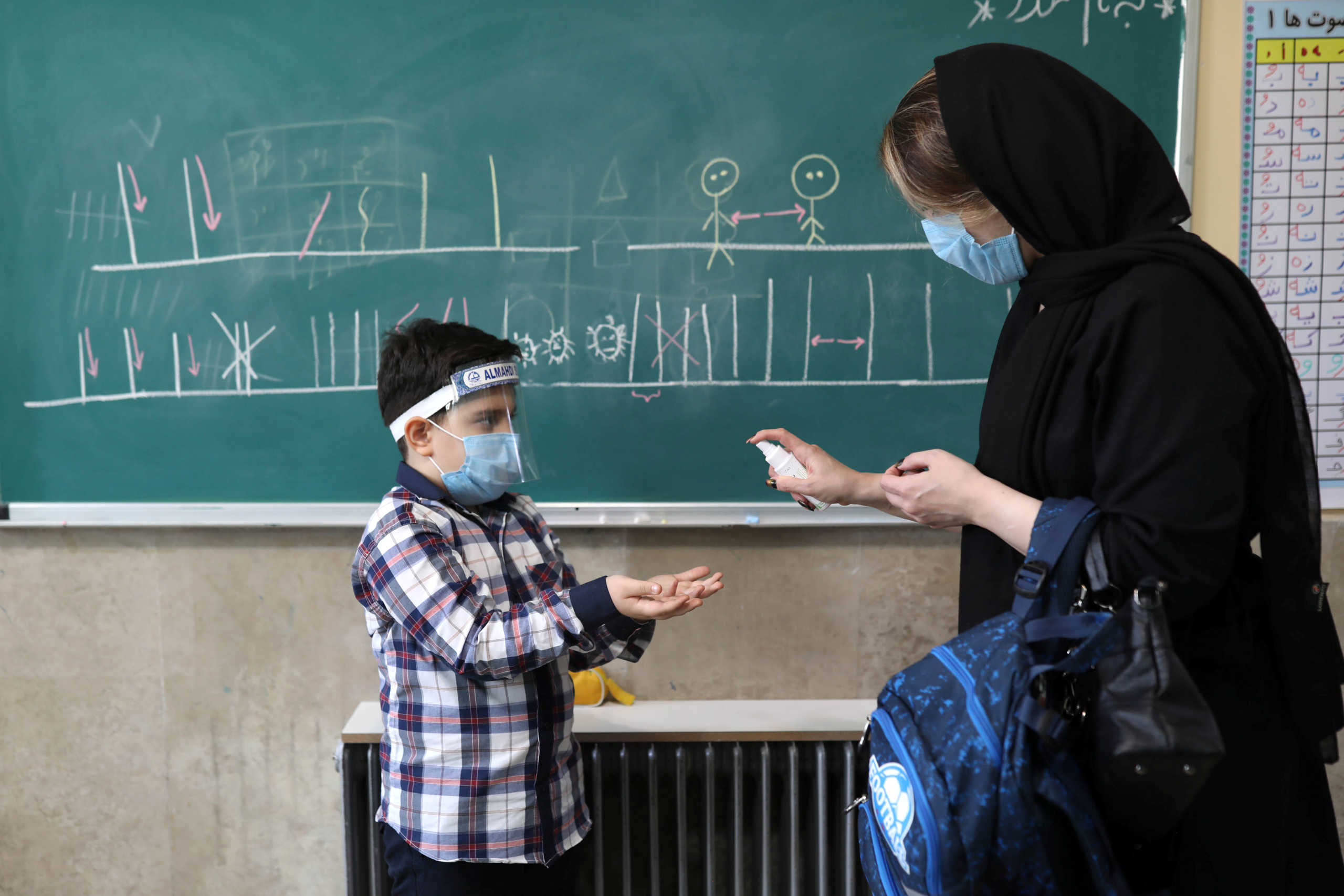 Mehrsam, a first-grade student, wears a protective face mask and shield to prevent the spread of the coronavirus disease (COVID-19), as his mother cleans his hands in a classroom at Al-Mahdi School in Tehran, Iran September 5, 2020. Picture taken September 5, 2020. Majid Asgaripour
