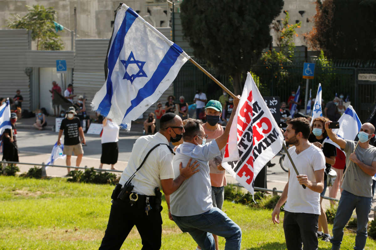 A policeman moves a protester as he waves an Israeli flag during a demonstration against the Israeli government as parliament resumes discussions to finalise legislation restricting demonstrations during the nation-wide coronavirus disease (COVID-19) lockdown, outside the Knesset, Israeli parliament, in Jerusalem September 29, 2020. REUTERS