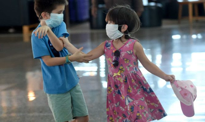 Two foreign children wearing facemasks play in front of the departure area of Ngurah Rai airport in Denpasar on February 8, 2020. - The new coronavirus that emerged in a Chinese market at the end of last year has killed more than 700 people and spread around the world. (Photo by SONNY TUMBELAKA