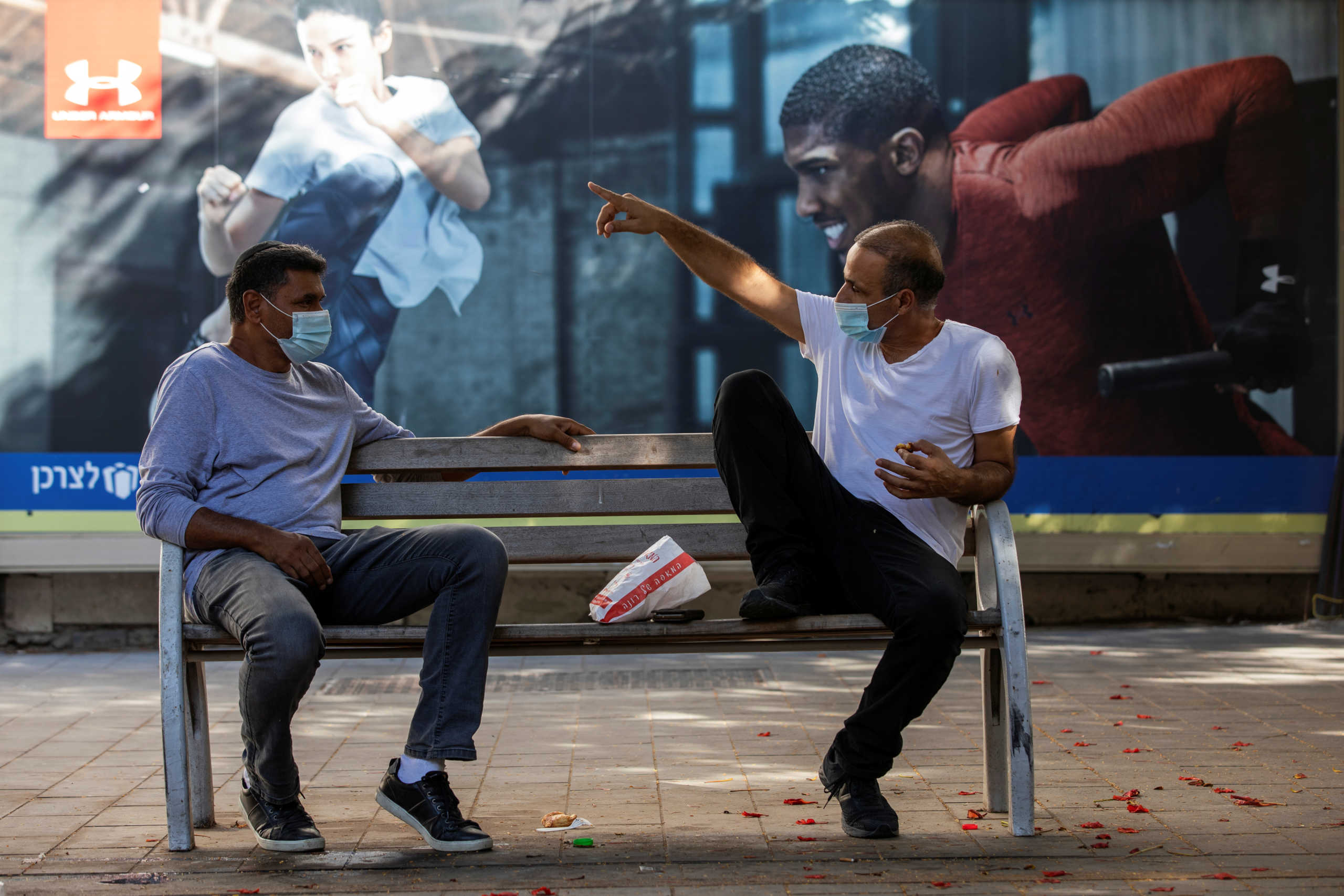 Men wearing protective face masks chat on a bench near shuttered shops amid Israel's second national coronavirus disease (COVID-19) lockdown in Ashkelon, Israel October 7, 2020. Picture taken October 7, 2020. REUTERS