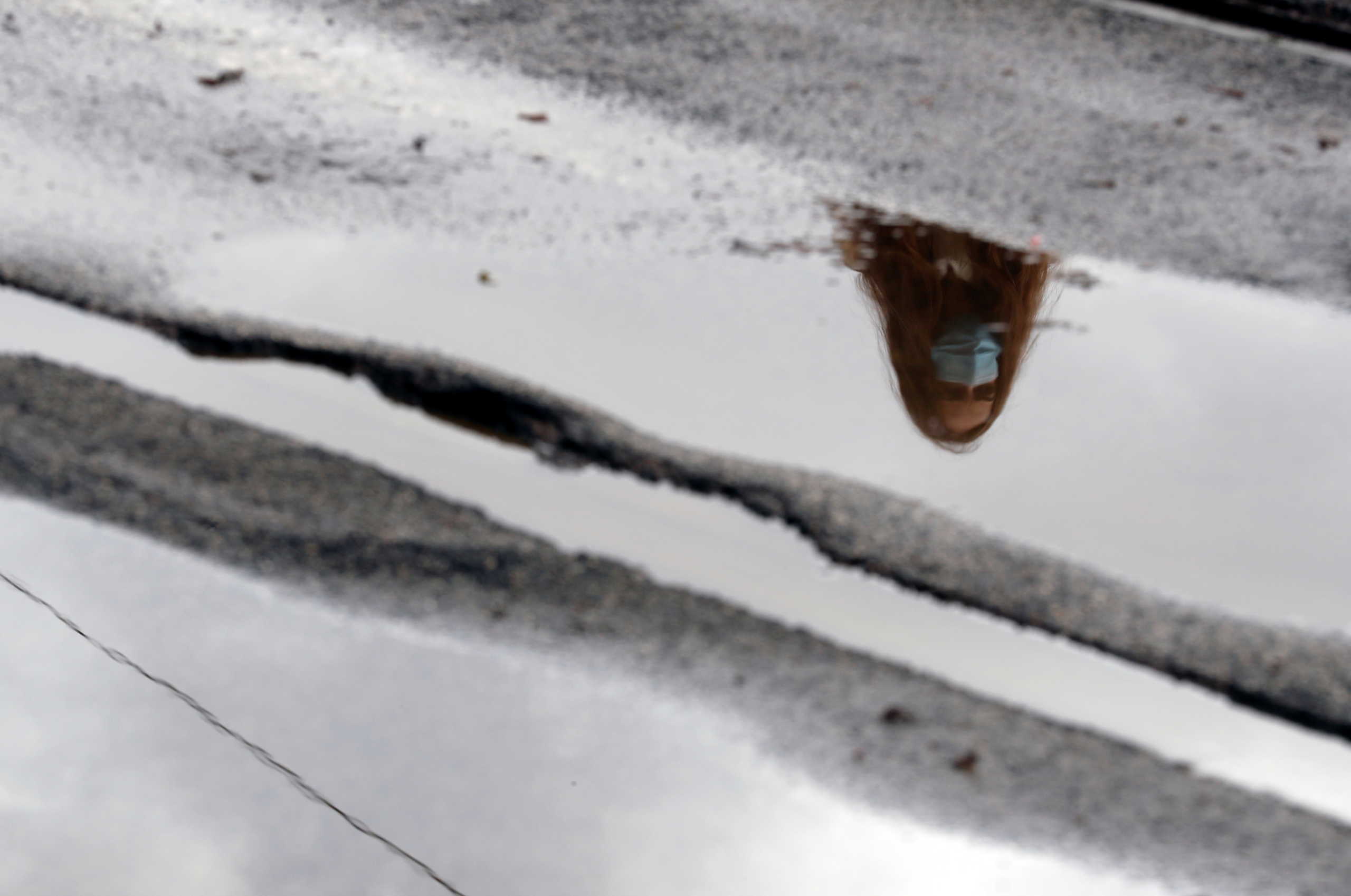 A woman wearing a face mask is reflected in a puddle as local authorities in the Italian capital order face coverings to be worn outdoors in an effort to counter the rising of the coronavirus disease (COVID-19) cases, in Rome, Italy, October 16, 2020. REUTERS