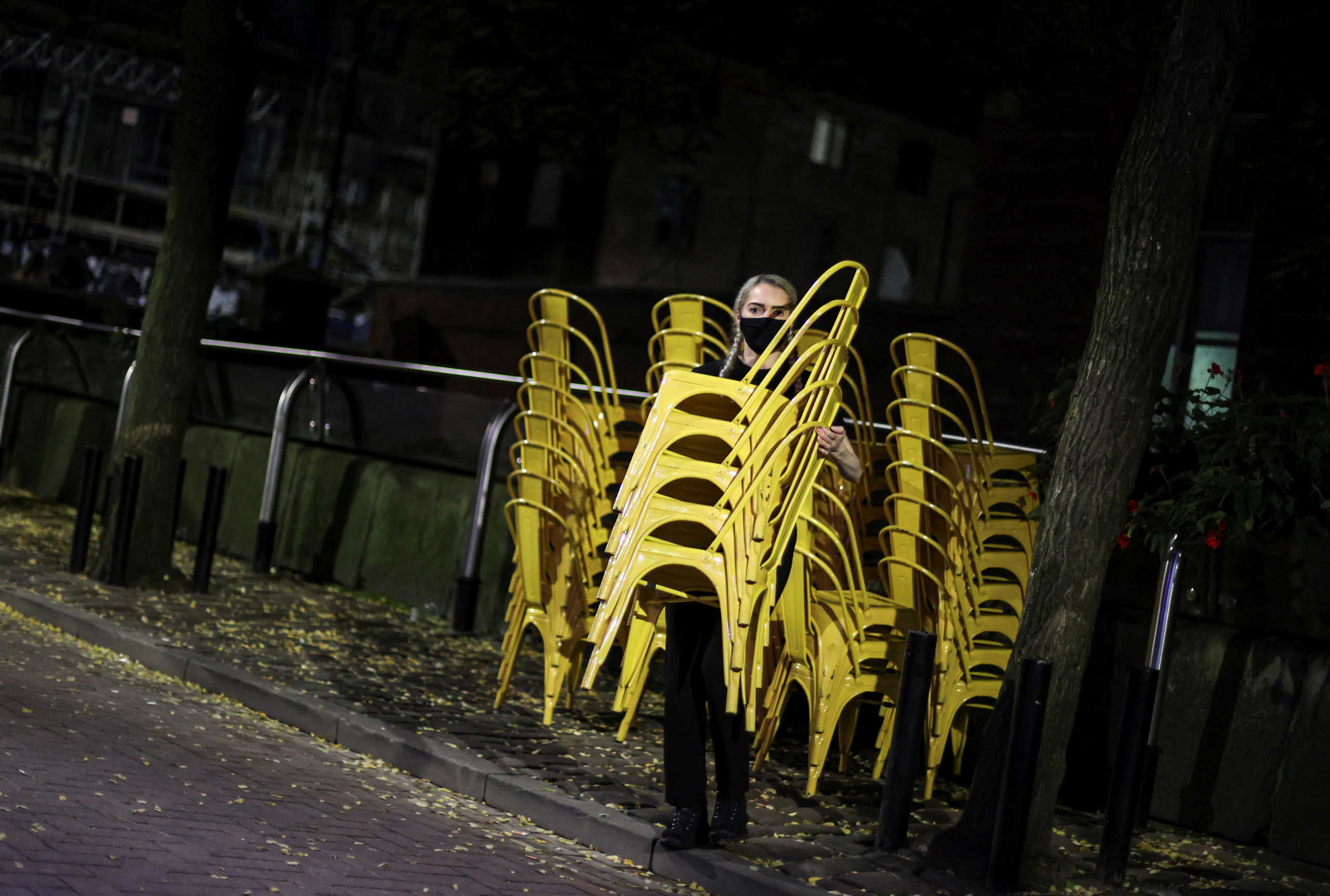 A woman wearing a face mask carries a load of chairs the night before a local lockdown amidst the spread of the coronavirus disease (COVID-19) in Manchester, Britain October 22, 2020. REUTERS