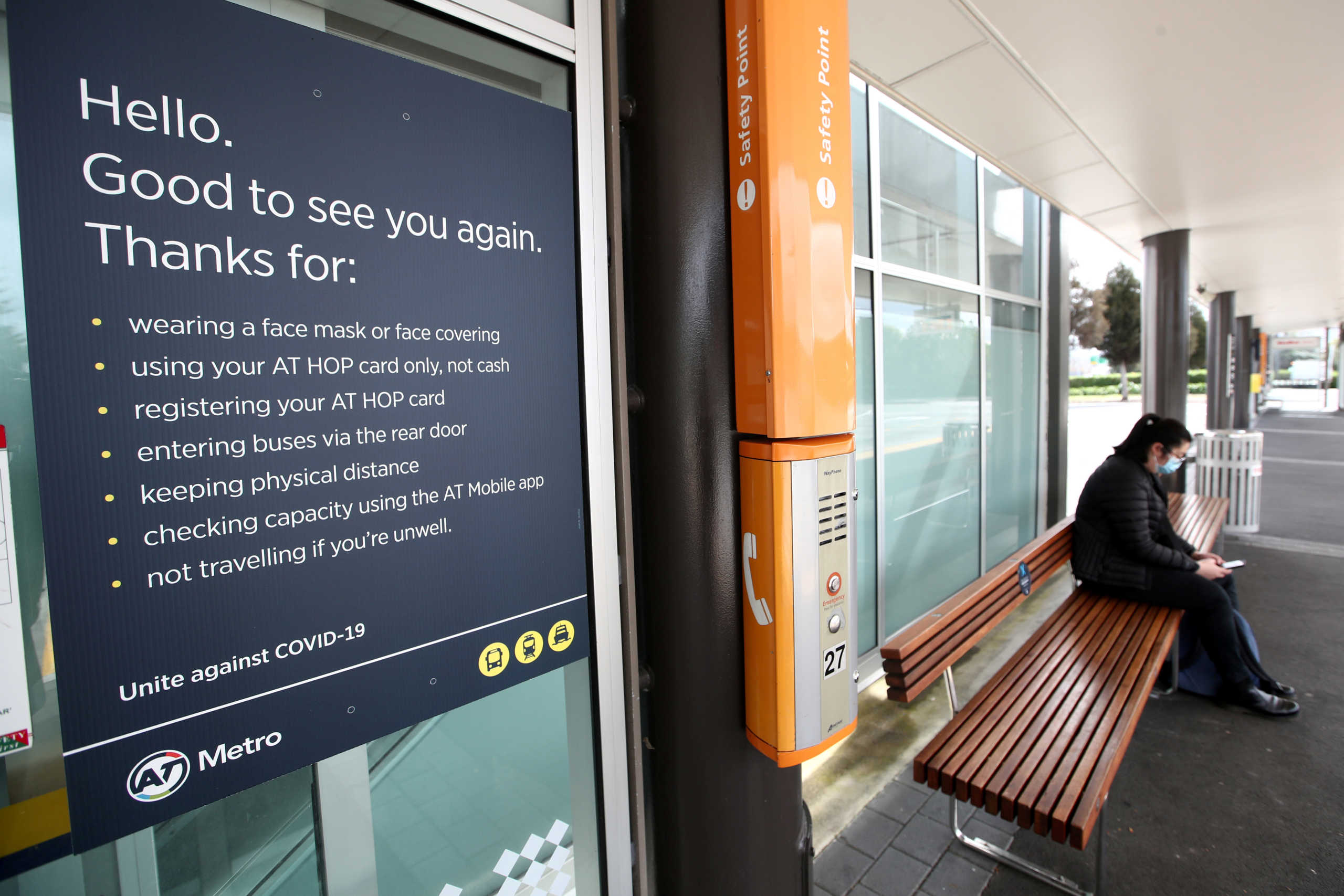 FILE PHOTO: A person wearing a face mask sits at a bus stop next to posted safety guidelines on the first day of New Zealand's new coronavirus disease (COVID-19) safety measure that mandates wearing of a mask on public transport, in Auckland, New Zealand, August 31, 2020.  REUTERS
