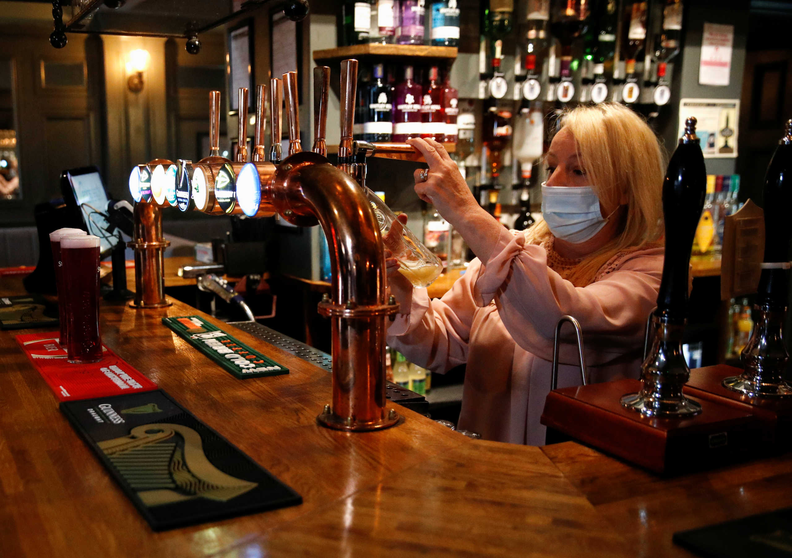 A woman wearing a face mask works behind a bar at the Grapes pub amid the outbreak of the coronavirus disease (COVID-19) in Liverpool, Britain, October 12, 2020. REUTERS