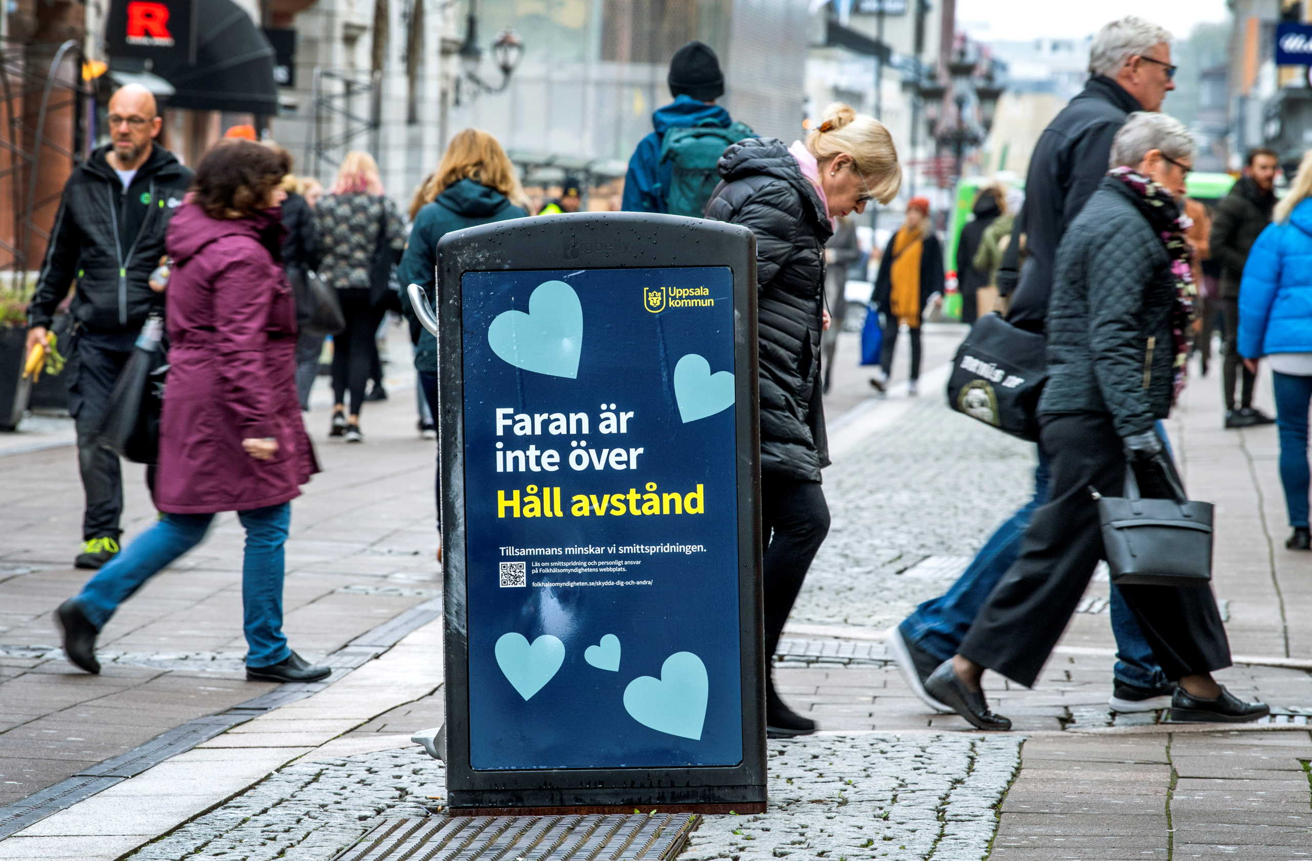 People walk near a trash can with a sign reading "The danger is not over - Keep your distance" on a pedestrian street as the coronavirus disease (COVID-19) outbreak continues in Uppsala, Sweden October 21, 2020. TT News Agency