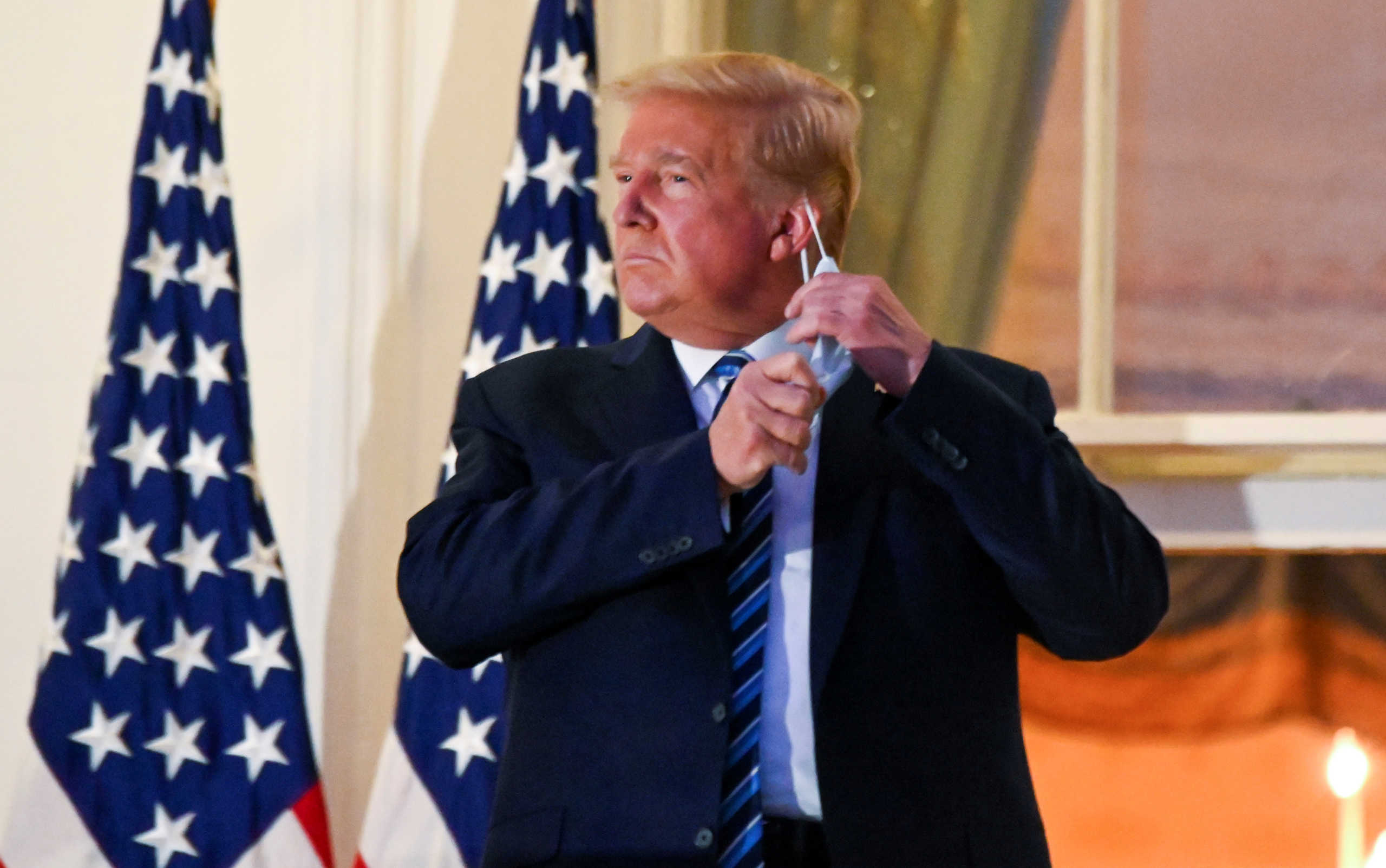 U.S. President Donald Trump pulls off his protective face mask as he poses atop the Truman Balcony of the White House after returning from being hospitalized at Walter Reed Medical Center for coronavirus disease (COVID-19) treatment, in Washington, U.S. October 5, 2020. REUTERS