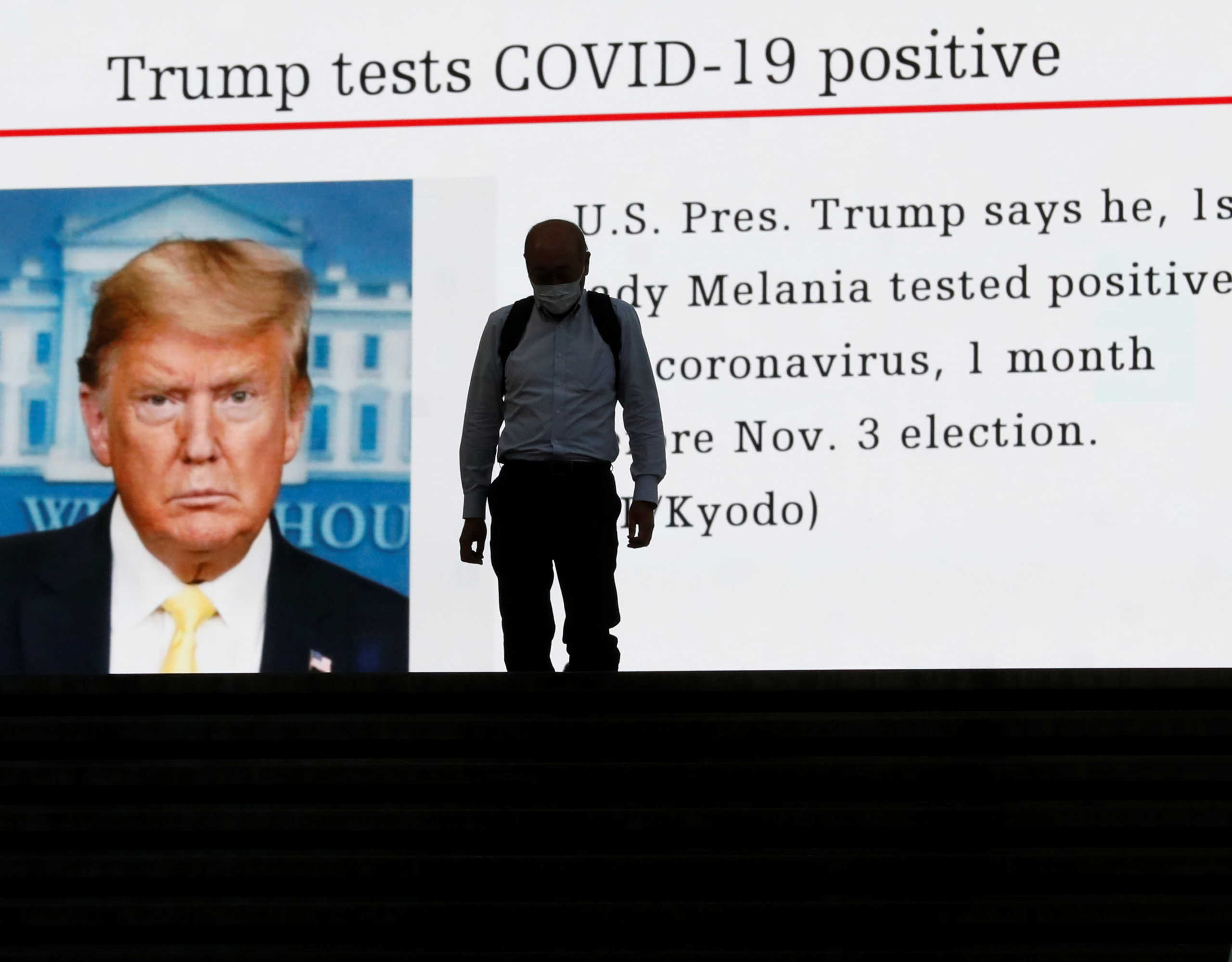 A man wearing a protective mask amid the coronavirus disease (COVID-19) outbreak, walks past a large screen showing a news about U.S. President Donald Trump who is tested positive for COVID-19 in Tokyo, Japan October 2, 2020. REUTERS