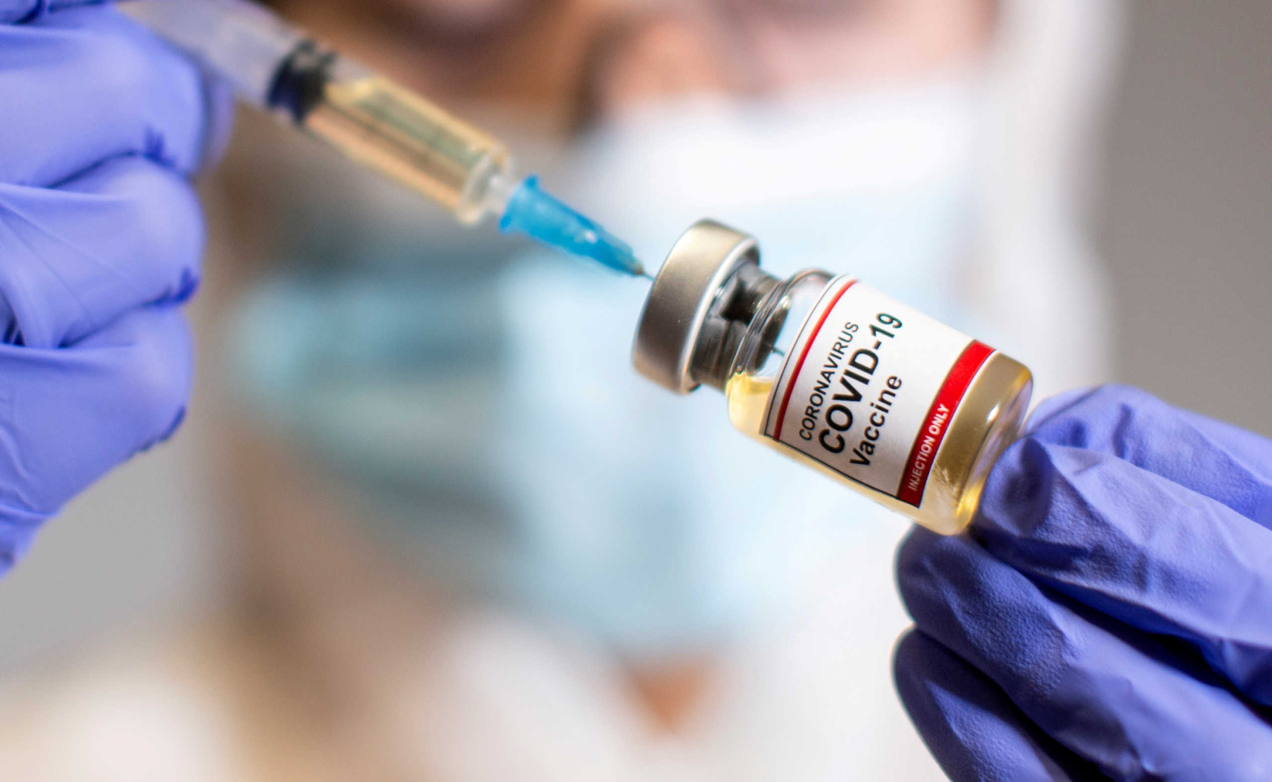 FILE PHOTO: A woman holds a small bottle labeled with a "Coronavirus COVID-19 Vaccine" sticker and a medical syringe in this illustration taken  October 30, 2020. REUTERS