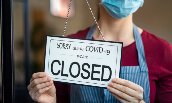 Businesswoman closing her business activity due to covid-19 lockdown. Owner with surgical mask close the doors of her store due to quarantine coronavirus damage. Close up sign of bankrupt business due to the effect of COVID-19 pandemic.