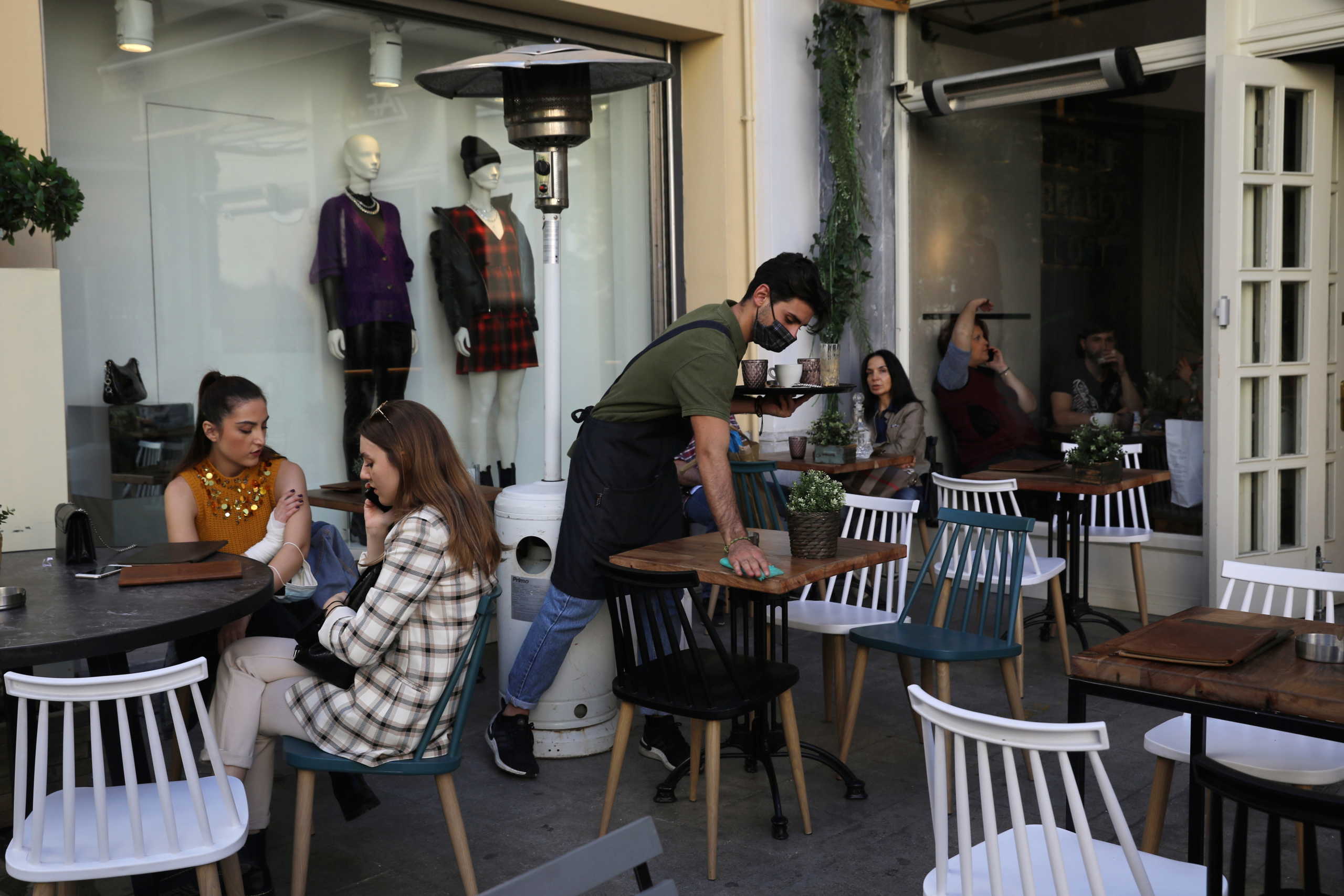 A waiter wearing a protective face mask cleans a table at a coffee shop, amid the spread of the coronavirus disease (COVID-19), in Athens, Greece, October 31, 2020. REUTERS