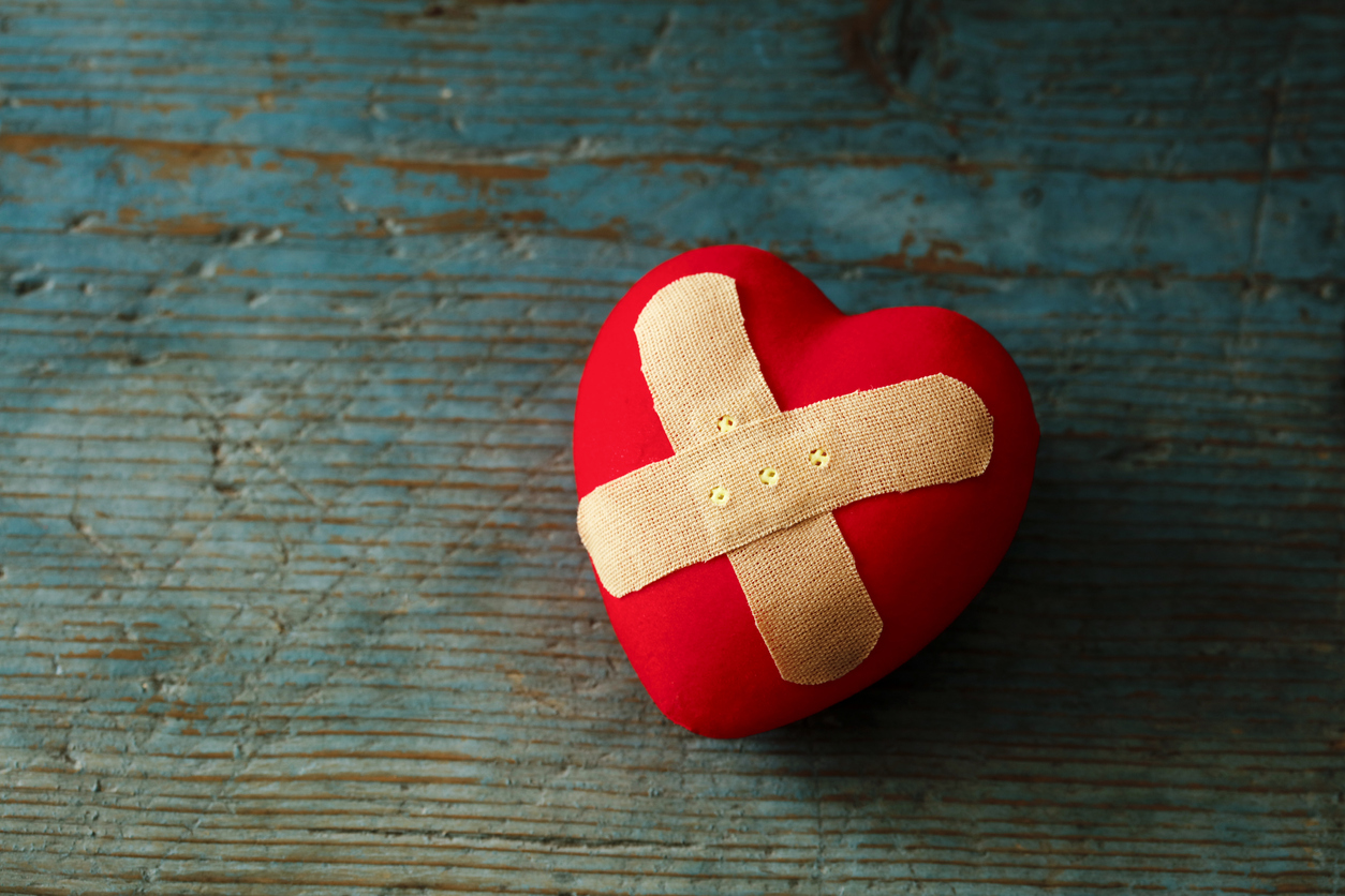 Band-aid covering a heart on a blue wooden background