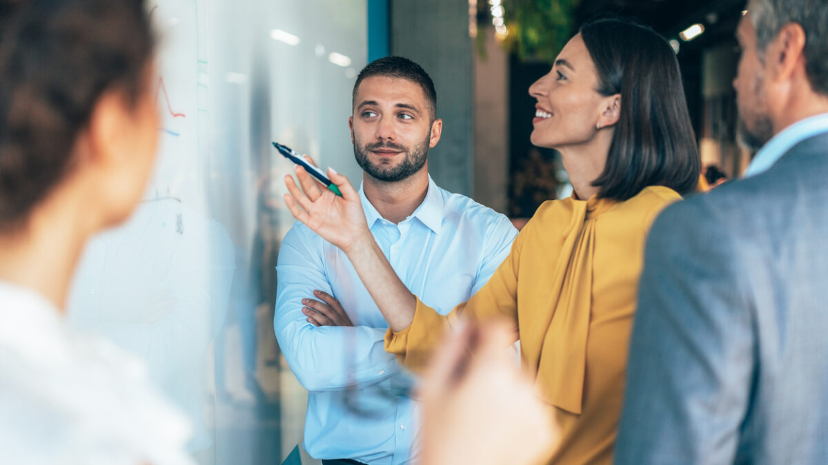 coworkers in a startup brainstorming strategies, writing a business plan on whiteboard to his team on a meeting