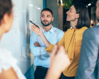 coworkers in a startup brainstorming strategies, writing a business plan on whiteboard to his team on a meeting