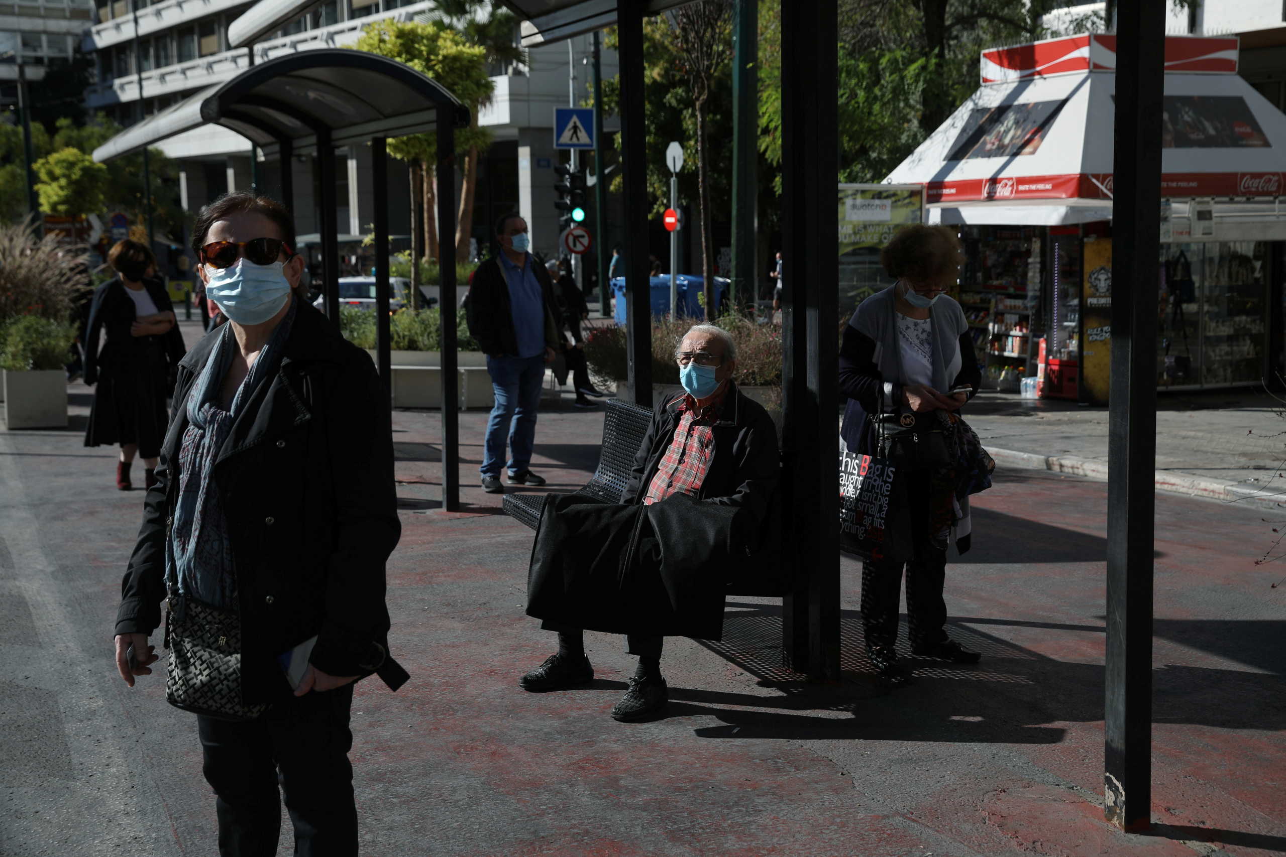 People wearing protective face masks wait for a bus at a bus stop, amid the spread of the coronavirus disease (COVID-19), in Athens, Greece, October 31, 2020. REUTERS