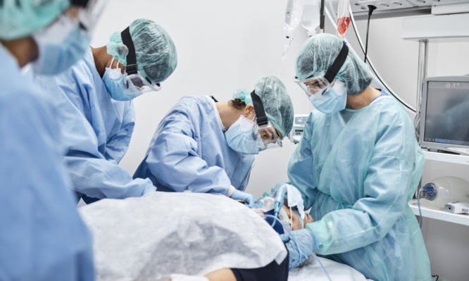 Team of doctors and nurses operating male patient in ICU. Frontline workers are treating man for coronavirus. They are in protective workwear.