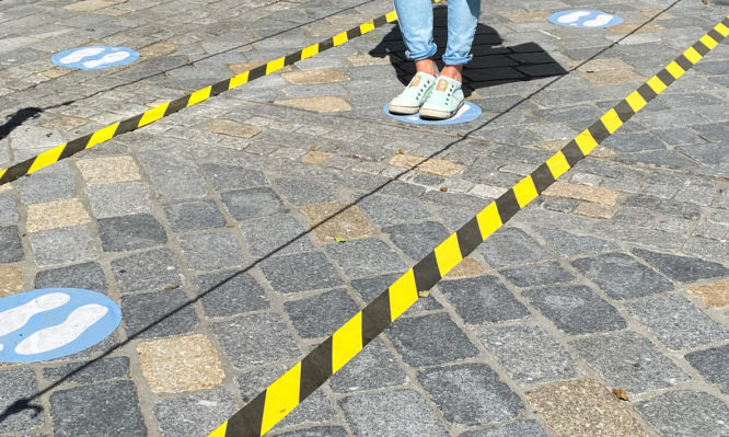 Roermond, Netherlands - May 19. 2020: View on feet of one person between do not cross tapes and blue markings to keep distance at shop entrance in corona crisis
