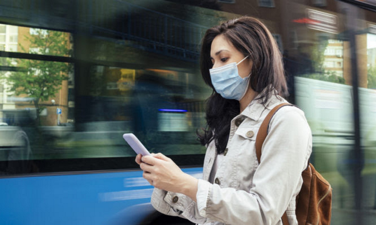 Woman standing in the bus stop. She is wearing a protective mask for the prevention of a virus. Coronavirus concept.