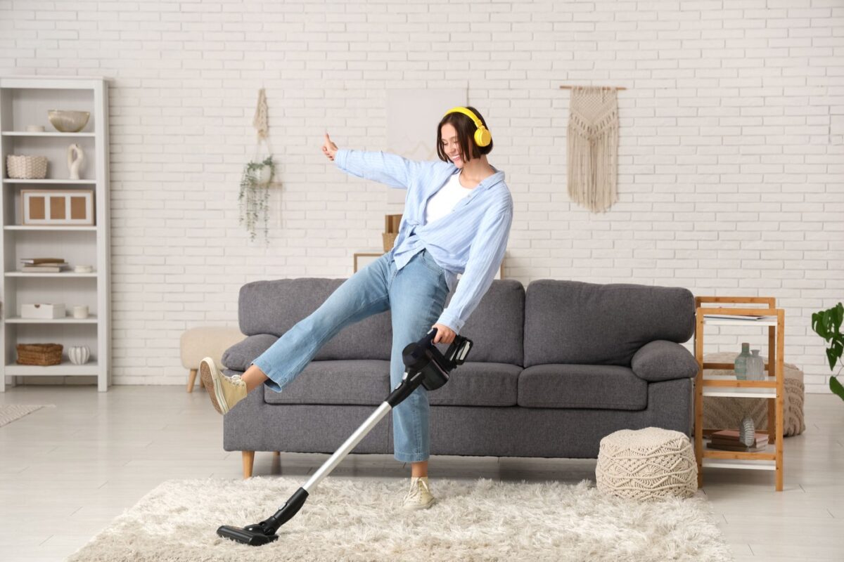 Beautiful young woman in headphones having fun with modern vacuum cleaner at home