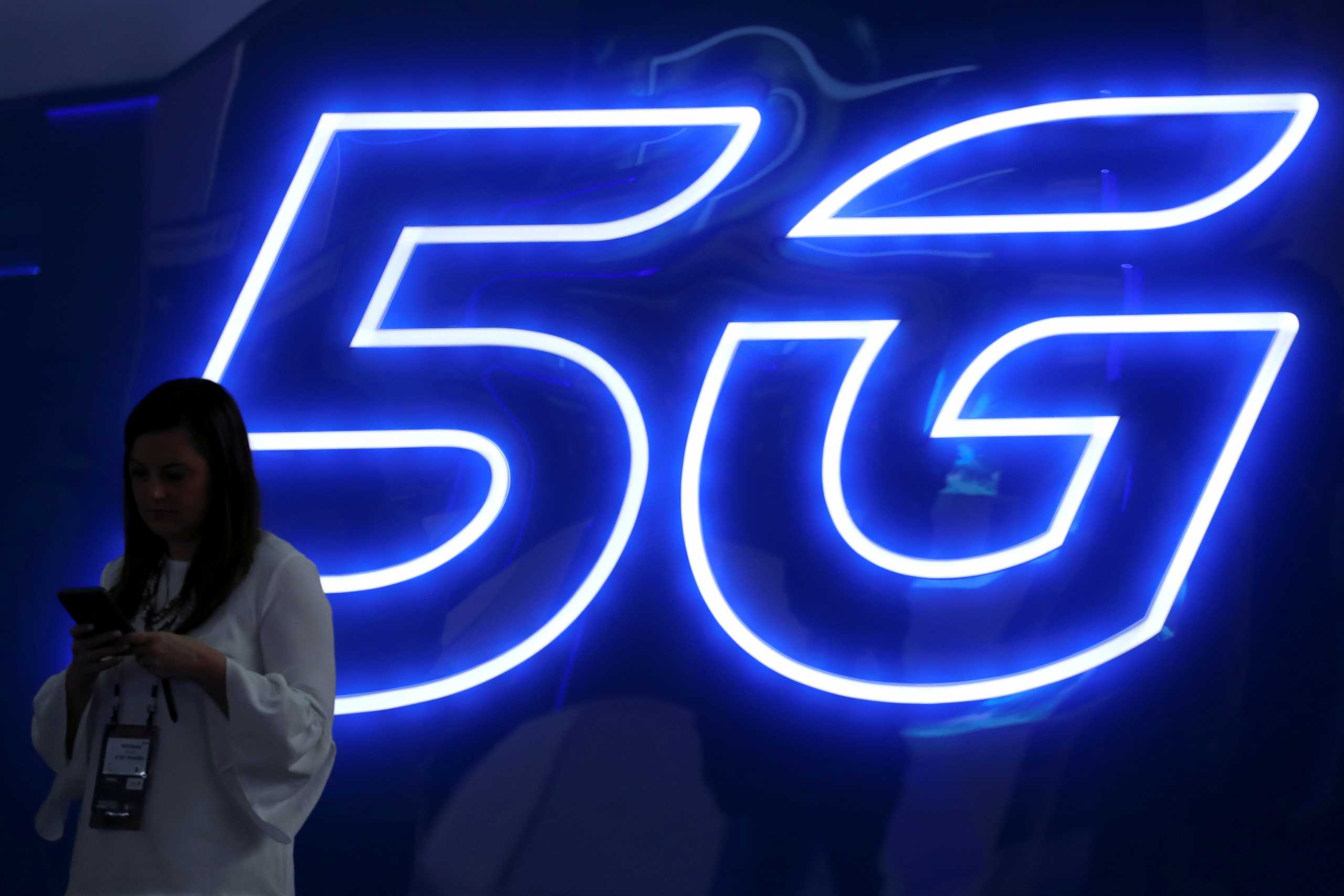 FILE PHOTO: A woman looks at her mobile phone next to a 5G sign at the Mobile World Congress in Barcelona, Spain, February 25, 2019. REUTERS