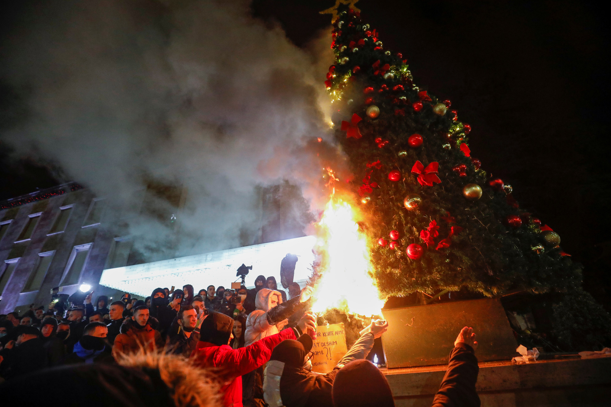 Demonstrators set fire to a Christmas tree in front of the prime minister's office during a protest in reaction to the death of Klodian Rasha, after he was shot dead during the country's overnight curfew, in Tirana, Albania, December 9, 2020. REUTERS