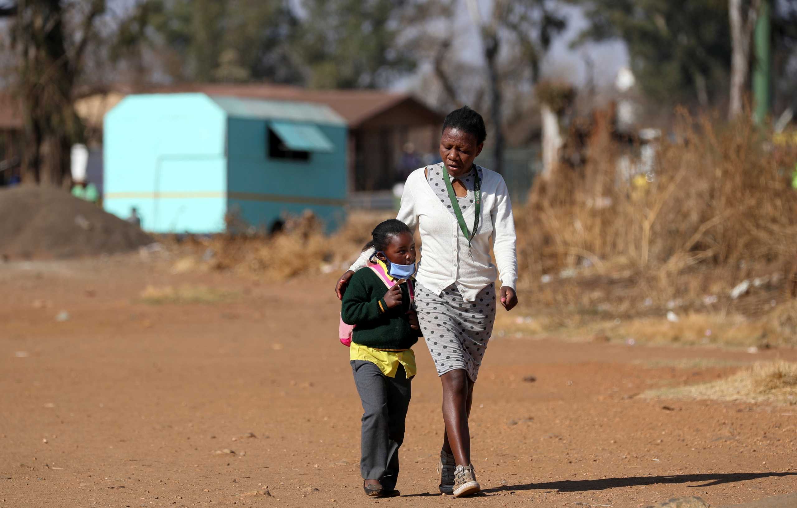 FILE PHOTO: A woman walks with her daughter as schools reopen amid a nationwide coronavirus disease (COVID-19) lockdown in Eikenhof, south of Johannesburg, South Africa August 24, 2020. REUTERS