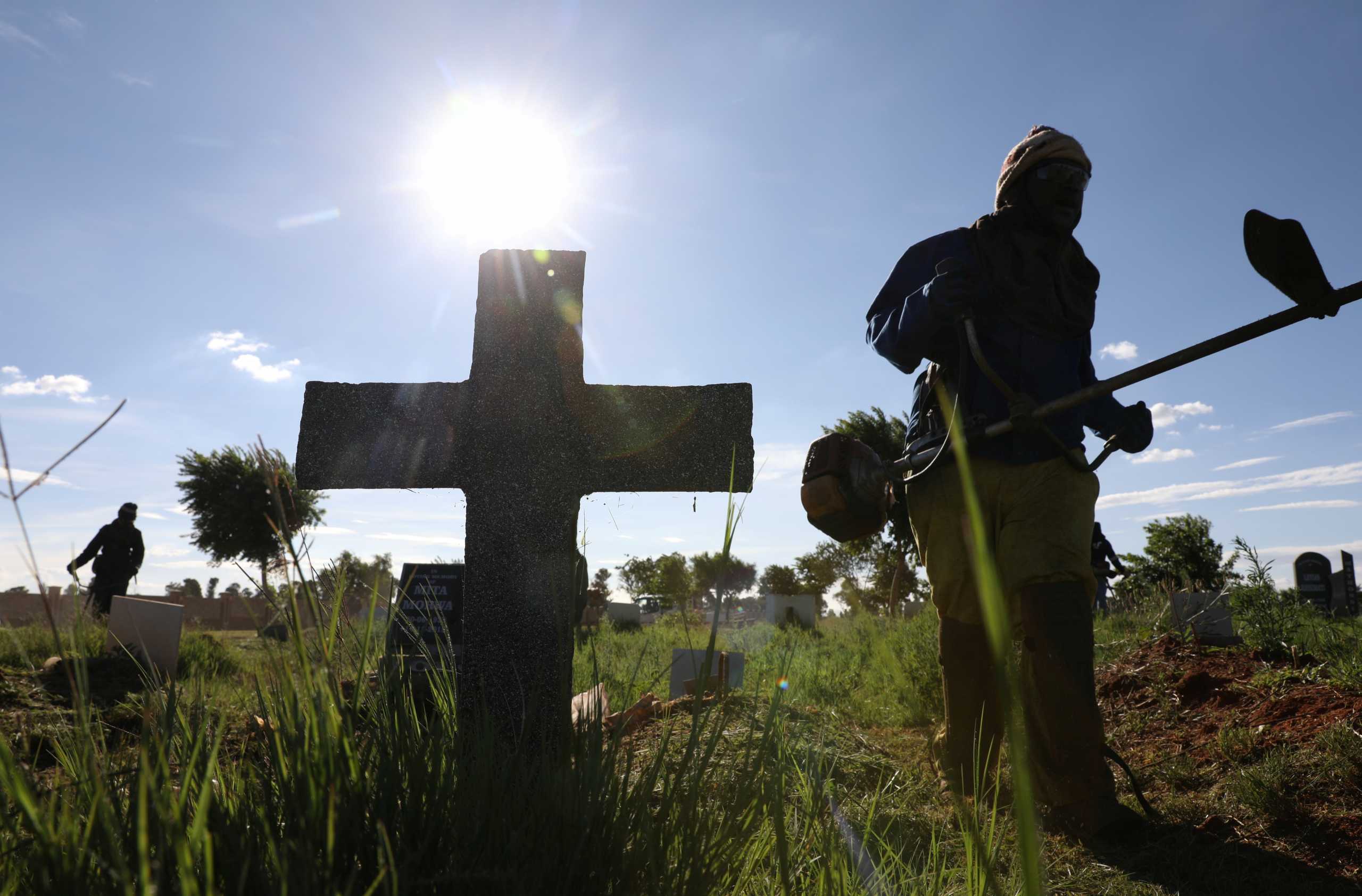 A cross marking a grave site is seen while a municipality worker cuts grass, as South Africa experiences a new variant of the coronavirus that is driving a second wave of infections, at Olifantsvlei Cemetary, south of Johannesburg, South Africa, December 21, 2020. REUTERS