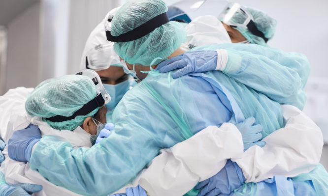 Medical professionals embracing each other in ICU. Doctors and nurses are in protective coveralls after successful treatment. They are at hospital during COVID-19.