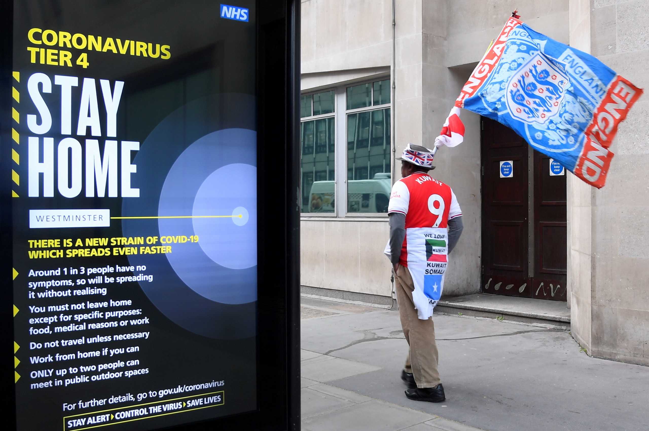 A man carrying a flag walks past a government public health message on a bus stop, amid the coronavirus disease (COVID-19) pandemic, in London, Britain December 30 2020. REUTERS