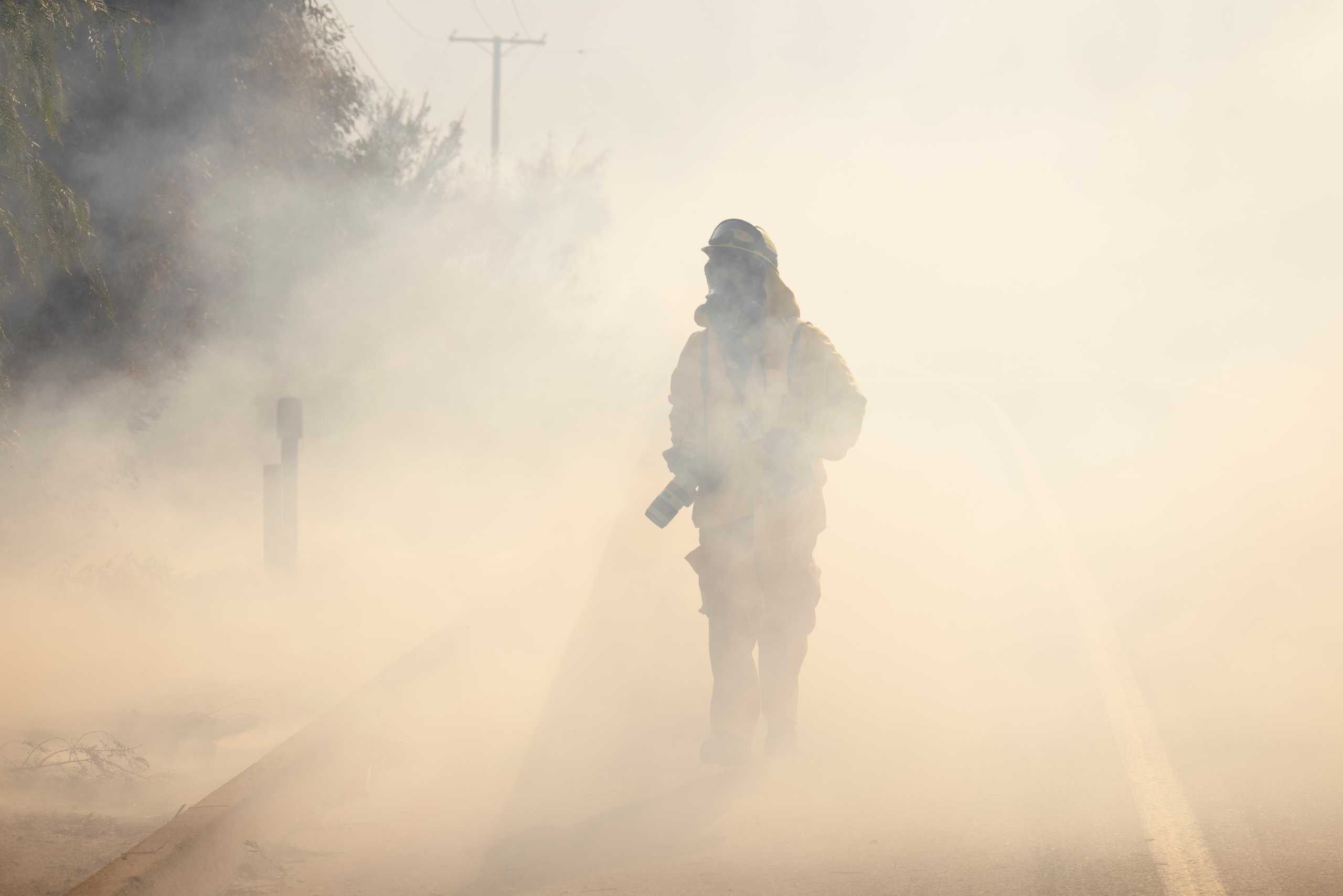 Los Angeles Times photojournalist  Allen J. Schaben makes his way through smoke as he works covering the wind driven Bond Fire wildfire near Lake Irvine in Orange County, California, U.S., December 3, 2020.  REUTERS