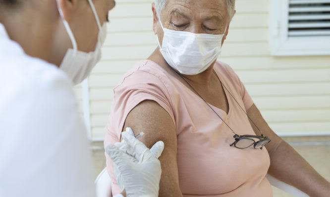 Senior woman wearing a protective face mask is getting vaccination from a female doctor with white surgical gloves and protective face mask.