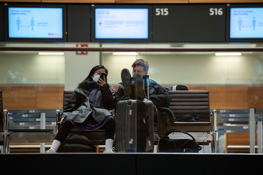 epa08897179 People sit and look at a phone in front of check-in counters at the Berlin Brandenburg Airport in Berlin, Germany, 21 December 2020. Concerned about a new and more contagious variant of the Corona virus, the German government, like many other European countries, has imposes a ban on flights from the United Kingdom to Germany.  EPA