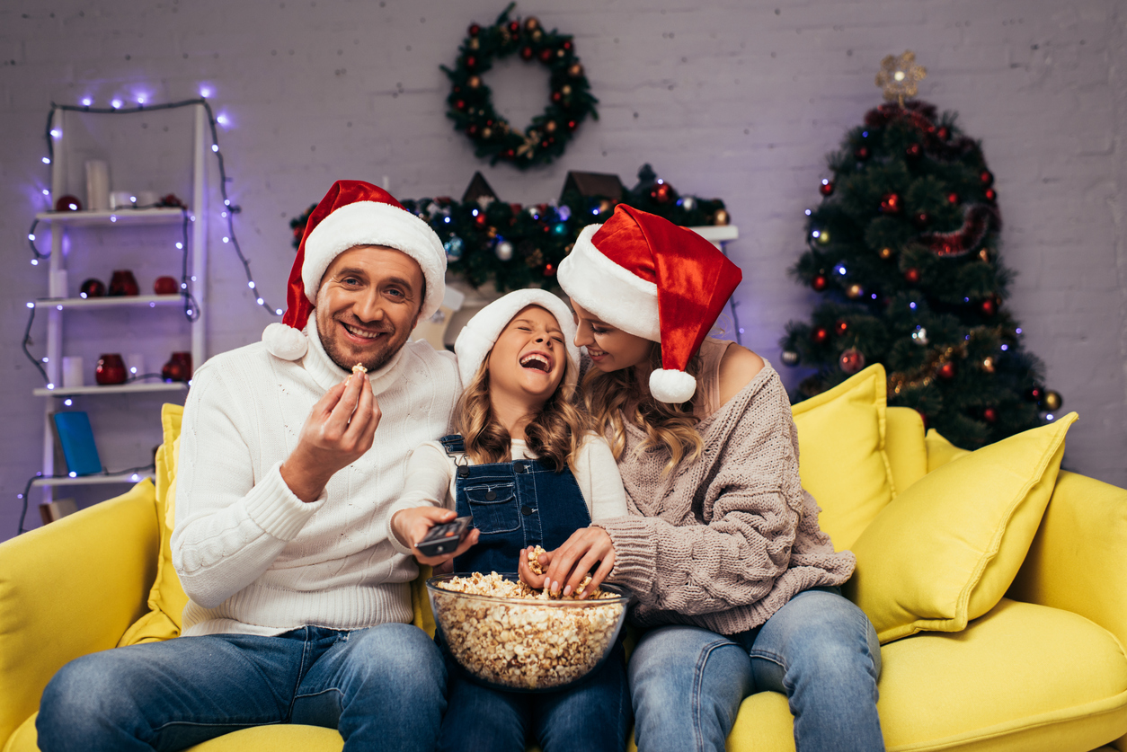 happy mother and daughter in santa hats laughing near man eating popcorn