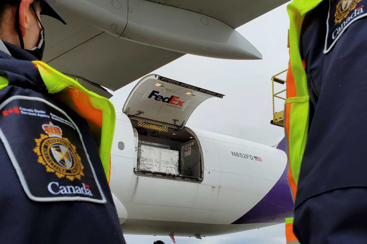 Canada Border Services Agency (CBSA) officers watch as the first shipment of newly authorized Moderna COVID-19 vaccine is unloaded from a Fedex cargo jet at a port of entry in Canada December 24, 2020.  Canada Border Services Agency