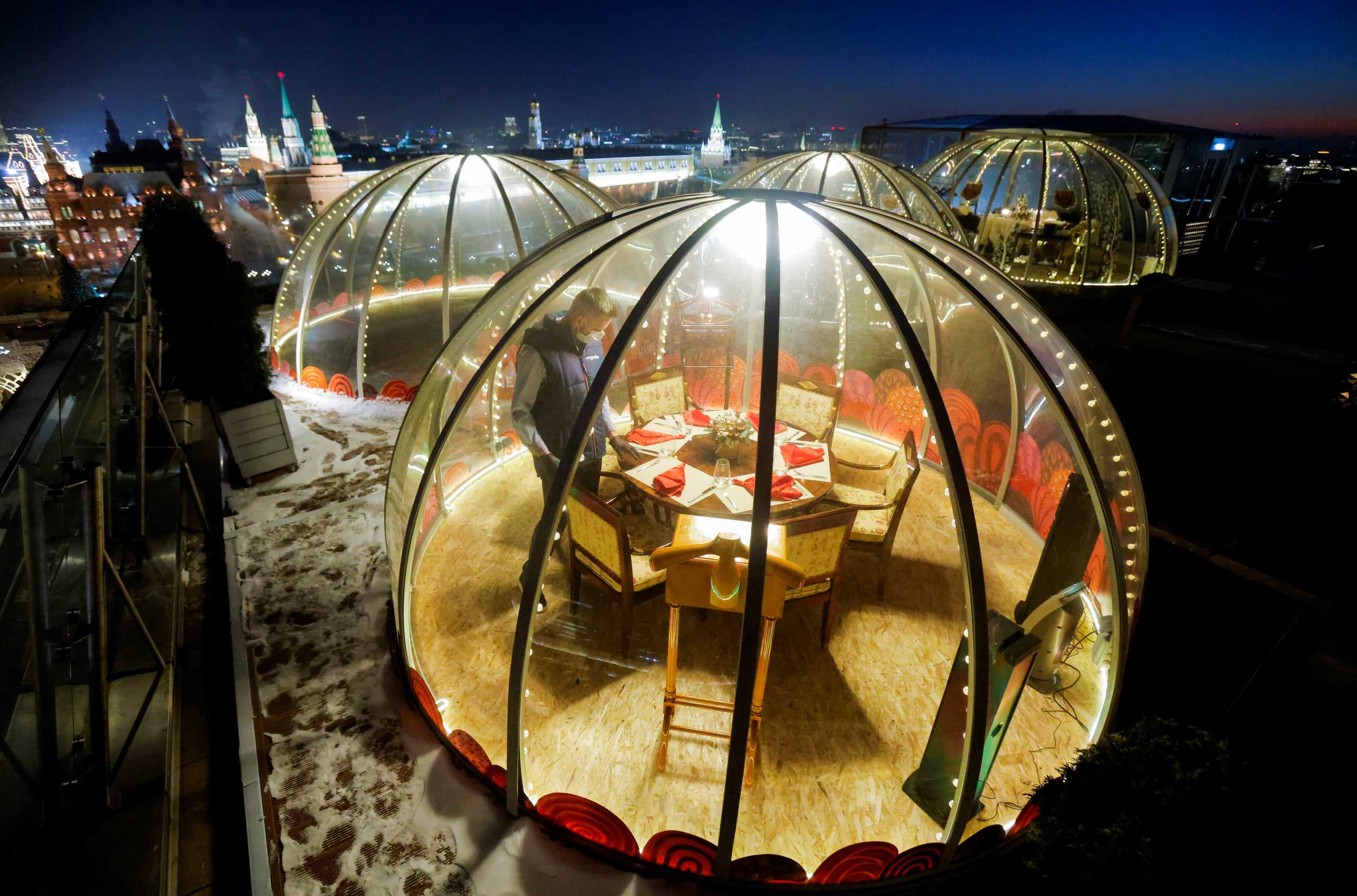 A waiter sets a table inside a transparent pod offered for private Christmas meals with backdrop of the Kremlin and Red Square on the rooftop of Ritz-Carlton hotel in Moscow, Russia December 8, 2020. Picture taken December 8, 2020. REUTERS