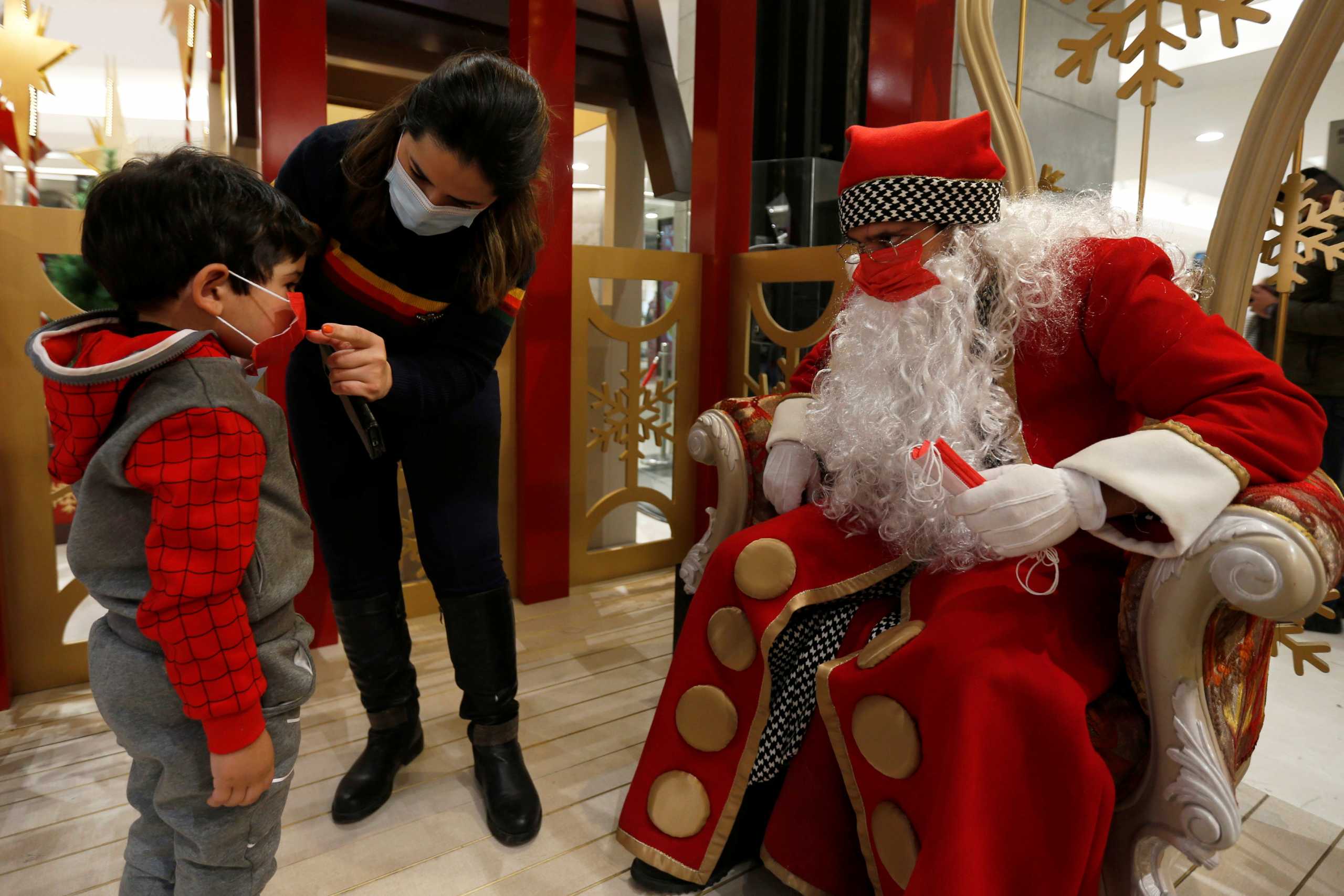A man dressed Santa Claus watches a child put on a mask before taking a picture with him ahead of Christmas at a mall,  amid fears over rising numbers of coronavirus disease (COVID-19) cases in Amman, Jordan December 15, 2020. REUTERS