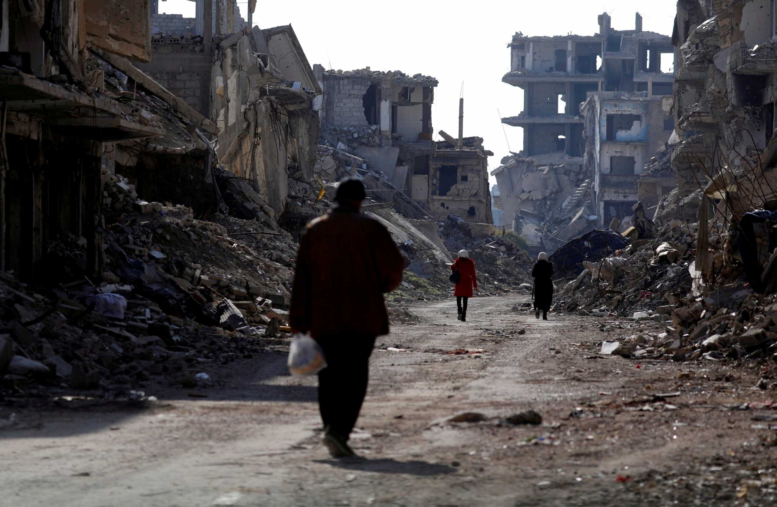 People walk past damaged buildings at the Yarmouk Palestinian refugee camp on the southern outskirts of Damascus, Syria December 2, 2020. Picture taken December 2, 2020. REUTERS
