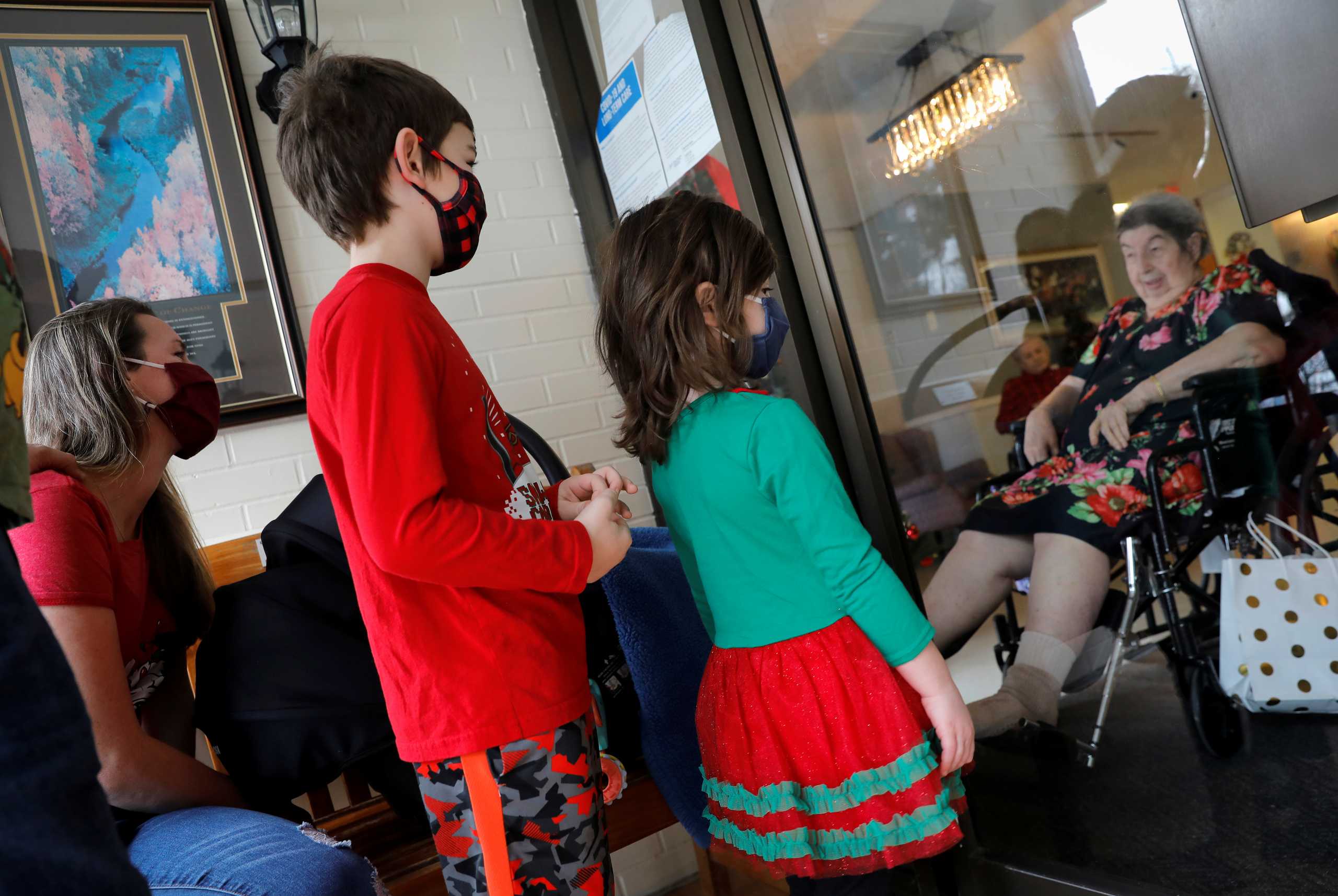 Four-year-old Riley Reynolds, her brother Michael (6) and their mother Christine pay a Christmas Eve visit through a glass window to the children's great-grandmother Lorraine Booth, a resident of the Tolstoy Foundation Rehabilitation and Nursing Center during the coronavirus disease (COVID-19) pandemic in Valley Cottage, New York, U.S., December 24, 2020. REUTERS