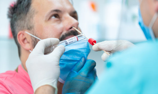 Doctor's hands in surgical gloves holding COVID-19 test kit and taking nasal swab from patient