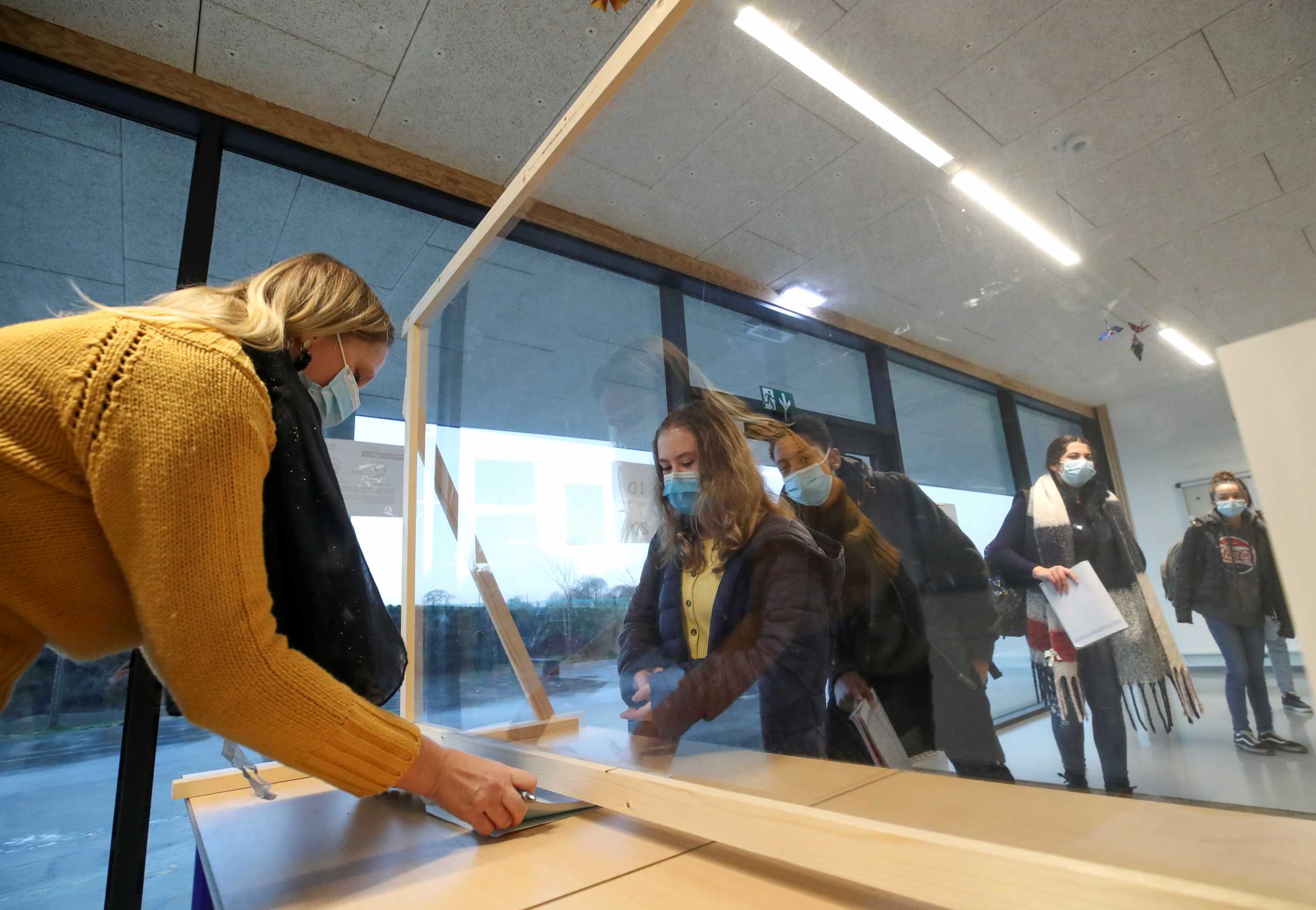 An employee wearing a protective face mask talks with a student behind a plastic barrier at a school amid the outbreak of the coronavirus disease (COVID-19), in Brussels, Belgium, December 16, 2020. REUTERS