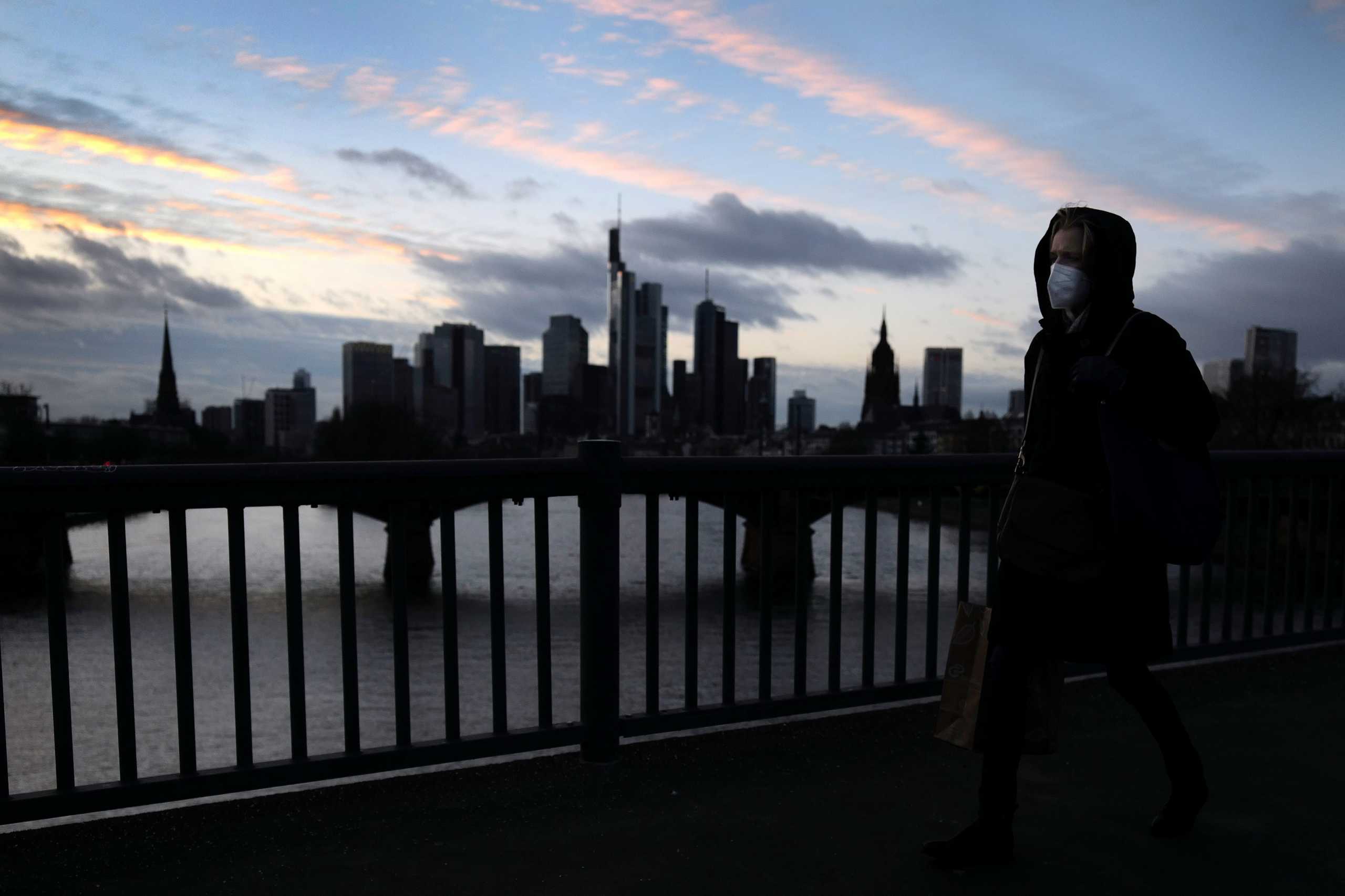 A woman wearing a protective mask crosses a bridge with a skyline backdrop as the spread of the coronavirus disease (COVID-19) continues during an extended lockdown in Frankfurt, Germany, January 13, 2021.  REUTERS