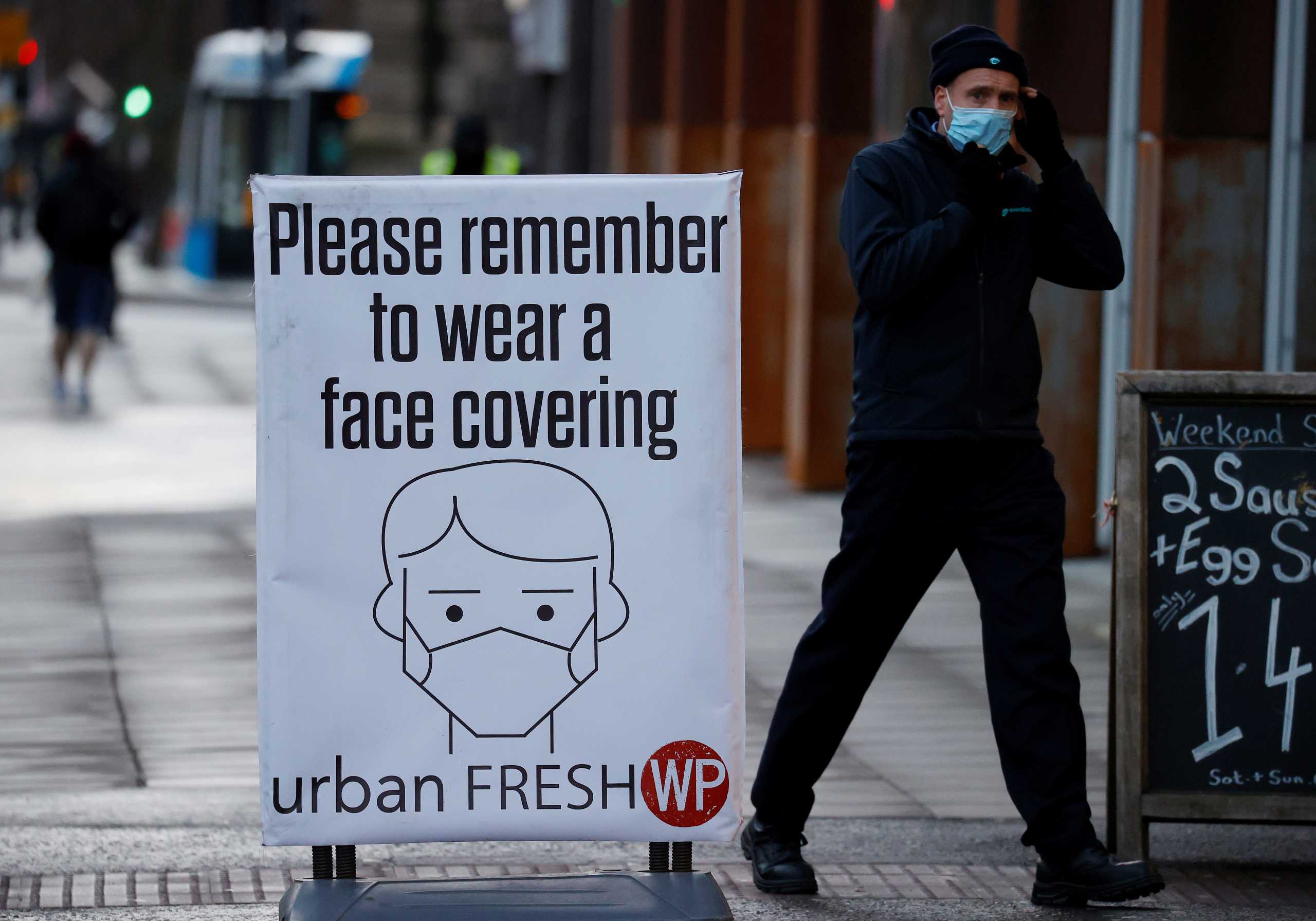 A man walks past a sign encouraging people to wear face coverings amid the COVID-19 outbreak in Belfast, Northern Ireland January 2, 2021. REUTERS