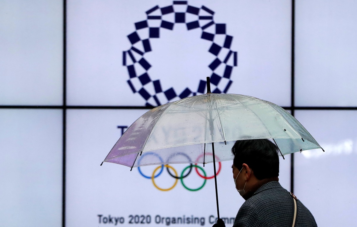 A man wearing a protective face mask walks past in front of a display showing the logo of Tokyo 2020 Olympic Games that have been postponed to 2021 due to the coronavirus disease (COVID-19) outbreak, in Tokyo, Japan January 23, 2021. REUTERS