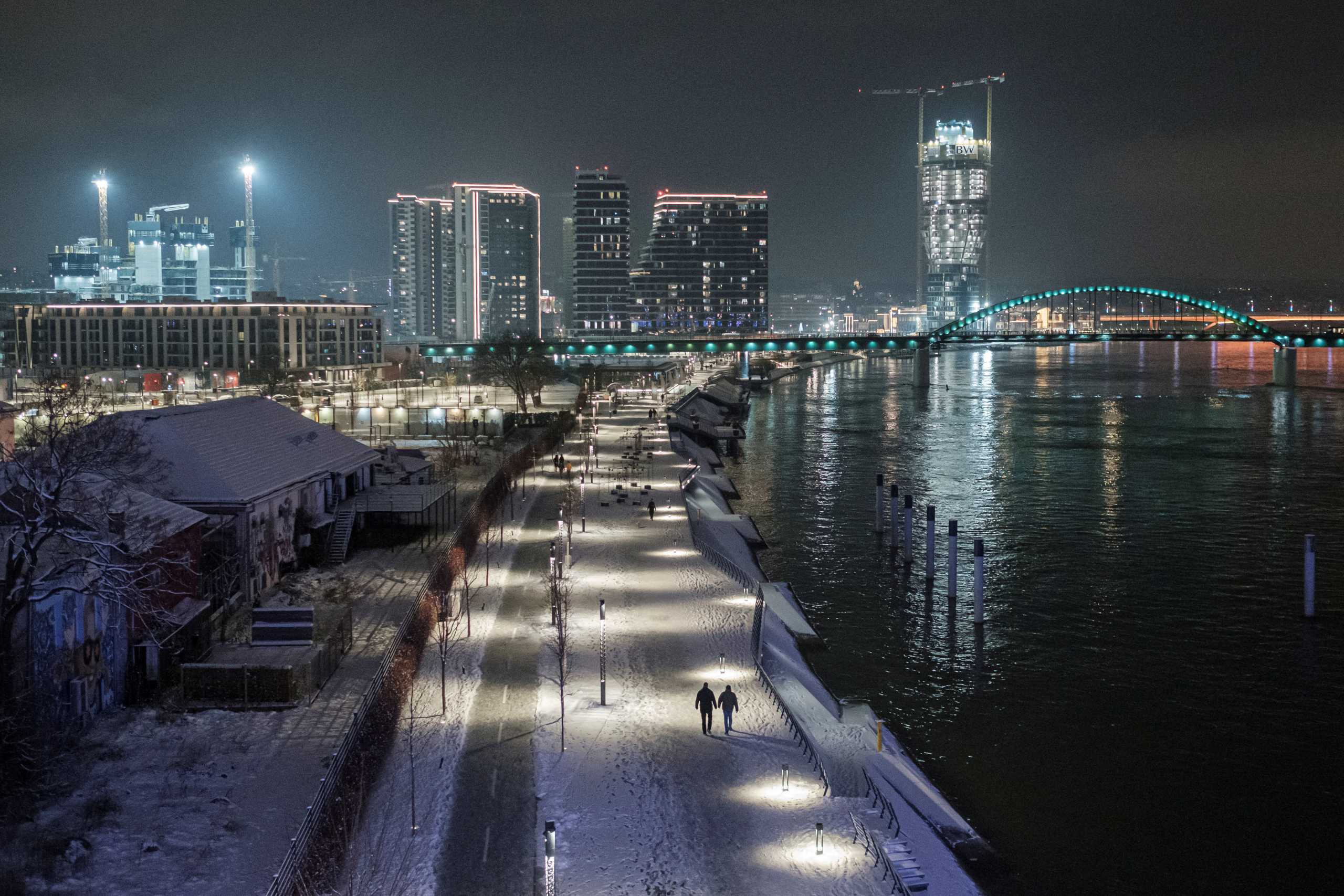 People walk on the banks of Sava river as the Belgrade Waterfront project is seen under construction in the background, in Belgrade, Serbia, January 17, 2021. REUTERS