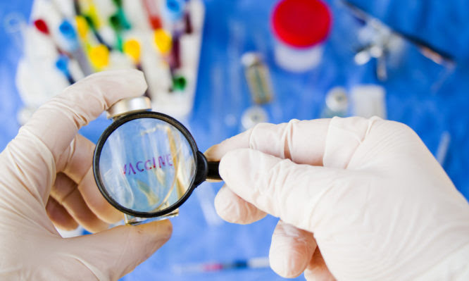 Corona virus and Covid - 19 new vaccine in ampules, doctor's hand whit white glove holding vaccine bottle and magnifying glass, looking and research. Laboratory situation.