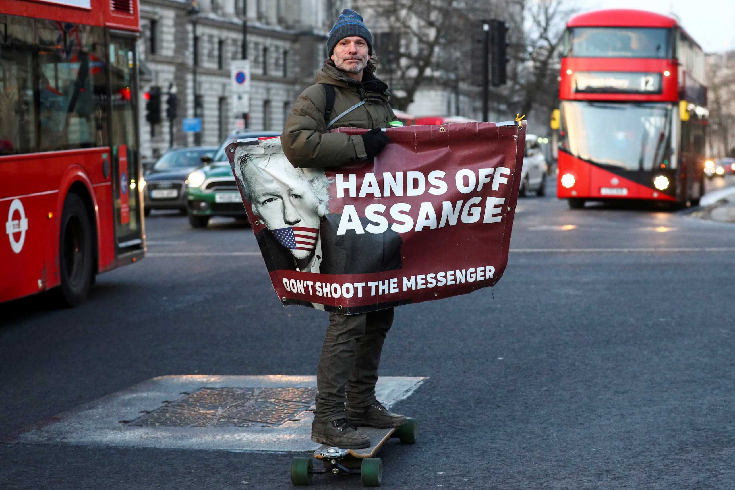 FILE PHOTO: A man rides a skateboard holding a banner with an image of Julian Assange in London, Britain, December 30, 2020. REUTERS