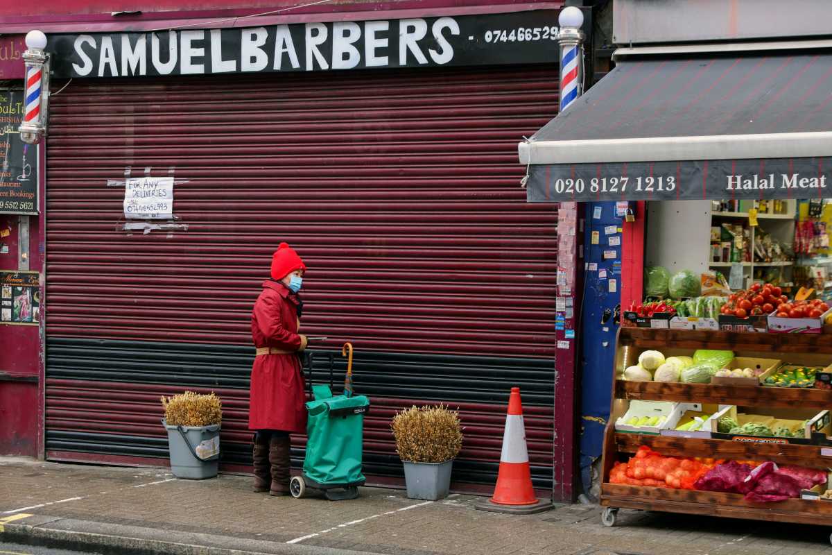 A woman wearing a face mask stands outside a closed barber shop as Britain began its third COVID-19 lockdown in Fulham, London, Britain, January 5, 2021.   REUTERS
