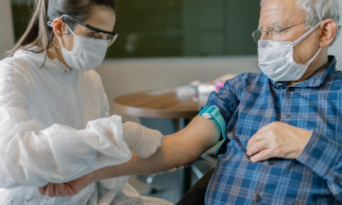 Female doctor wearing protective suit injecting vaccine into senior patient's arm