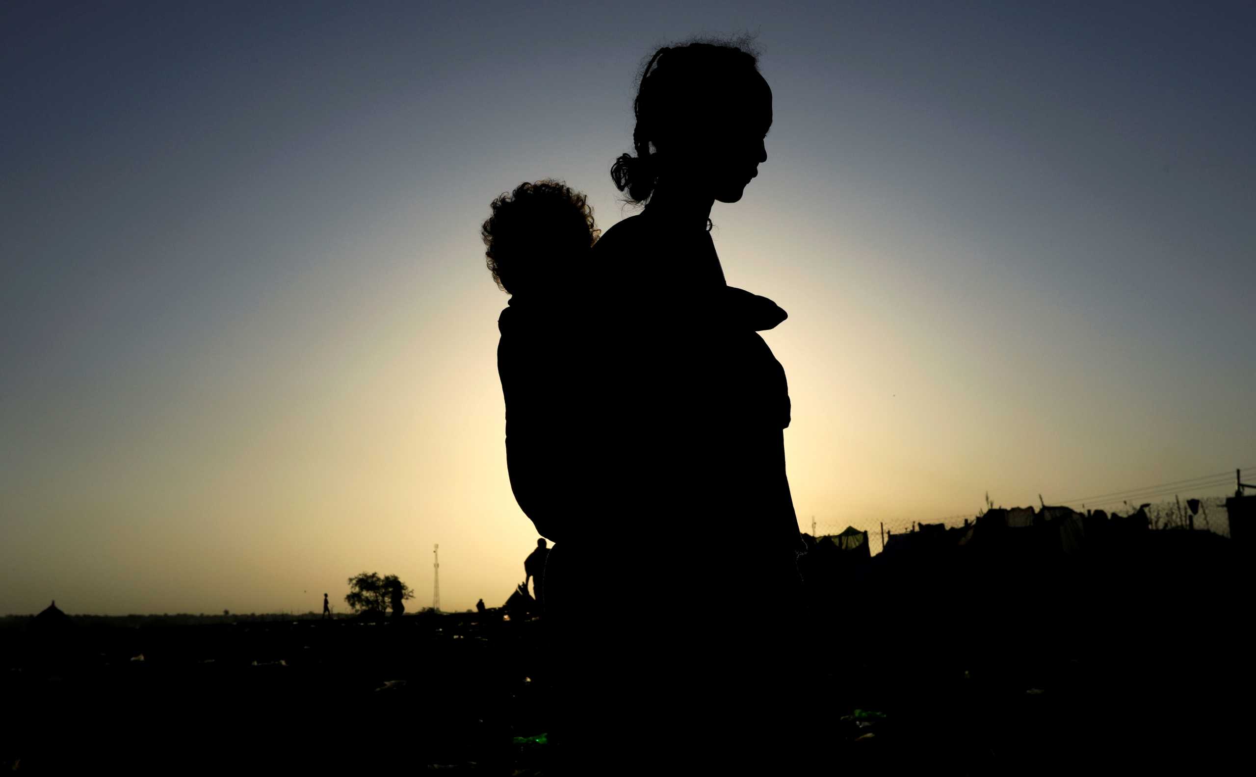FILE PHOTO: An Ethiopian woman who fled the ongoing fighting in Tigray region, carries her child near the Setit river on the Sudan-Ethiopia border in Hamdayet village in eastern Kassala state, Sudan November 22, 2020. REUTERS