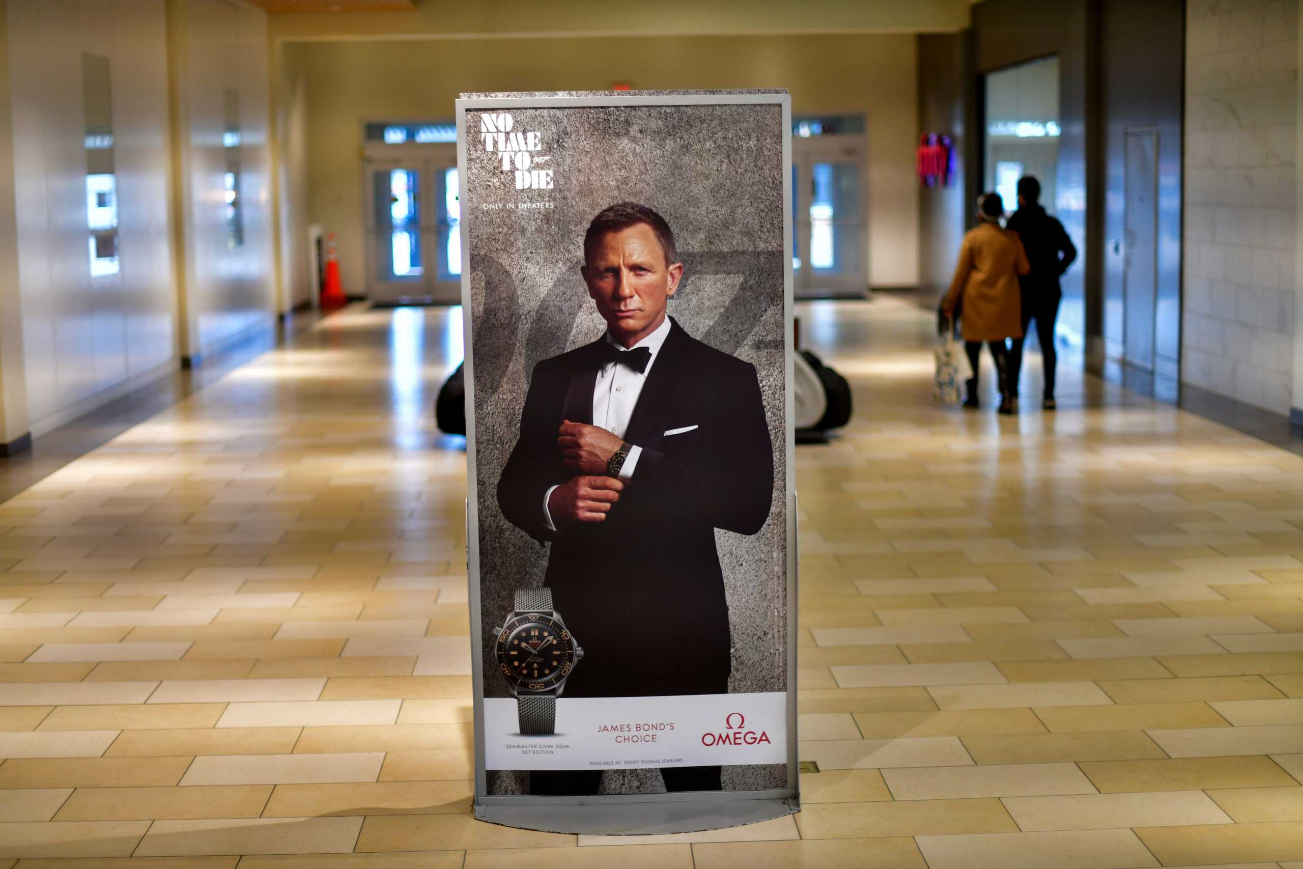 FILE PHOTO: Shoppers walk past an advertisement for the upcoming James Bond film "NO TIME TO DIE" whose release has been delayed due to the coronavirus disease (COVID-19) pandemic, at the Christiana Mall in Newark, Delaware U.S. November 19, 2020. REUTERS